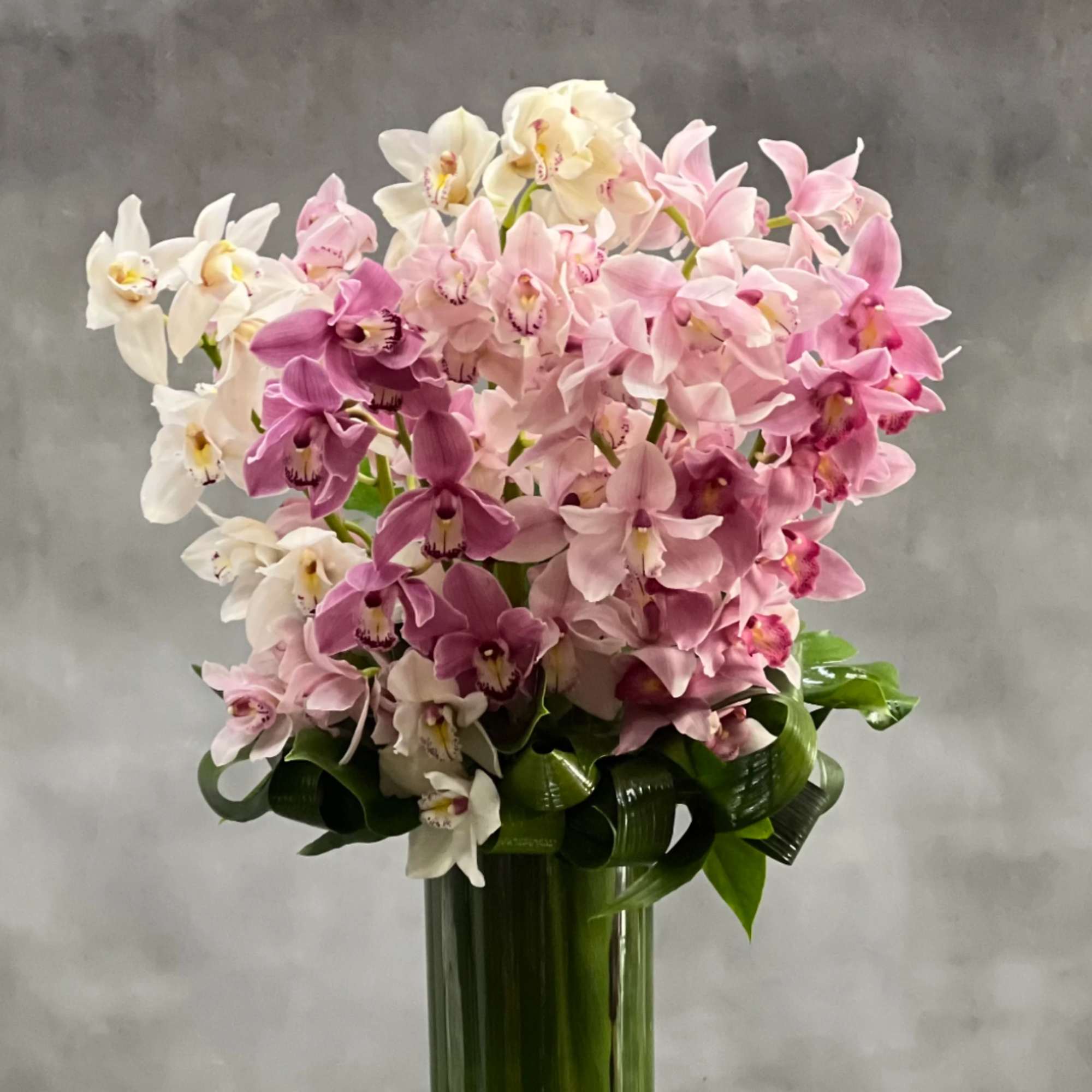 Tall arrangement of pink and white orchids in a green glass vase