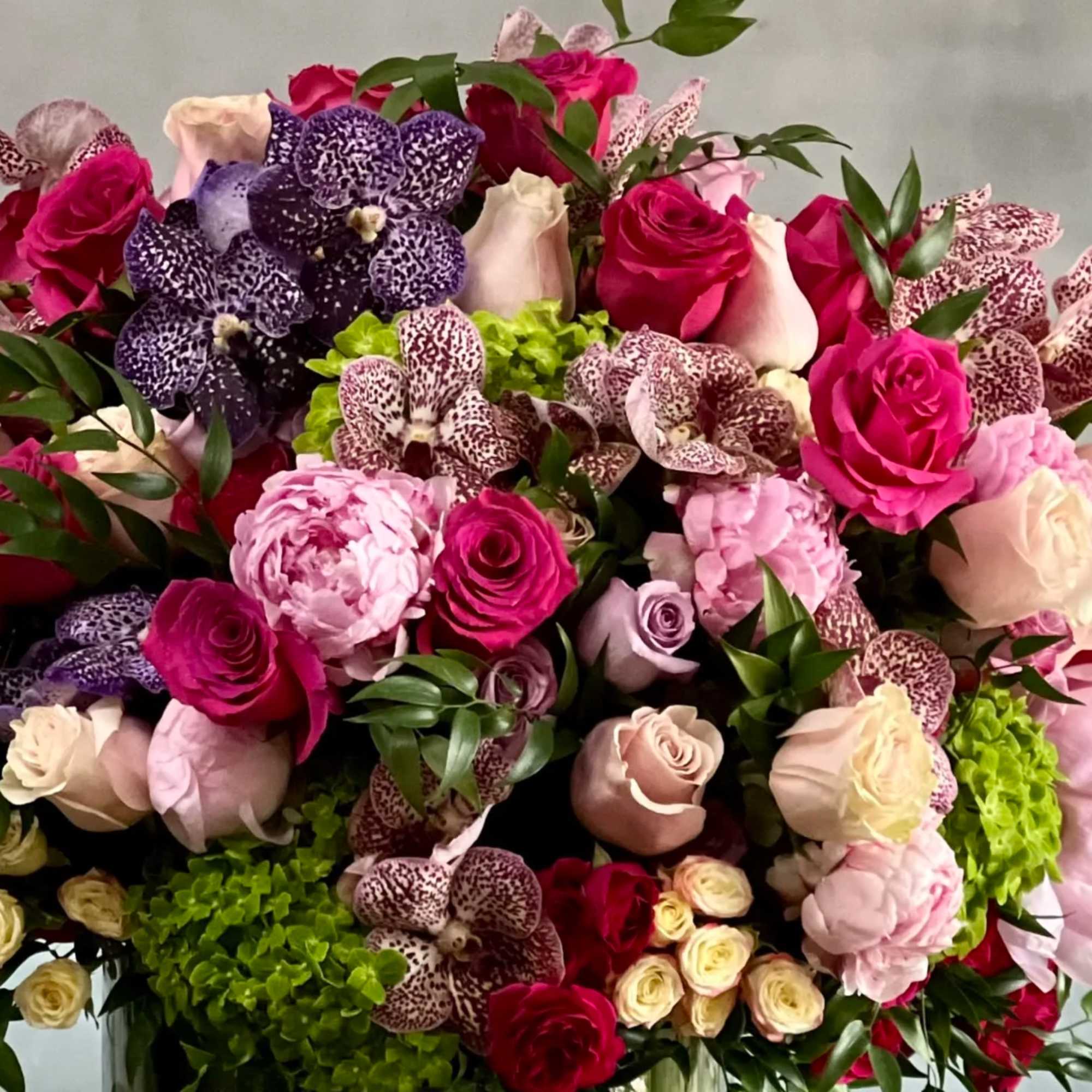 Lush arrangement of pink roses, peonies, orchids, and green hydrangeas in a dense cluster