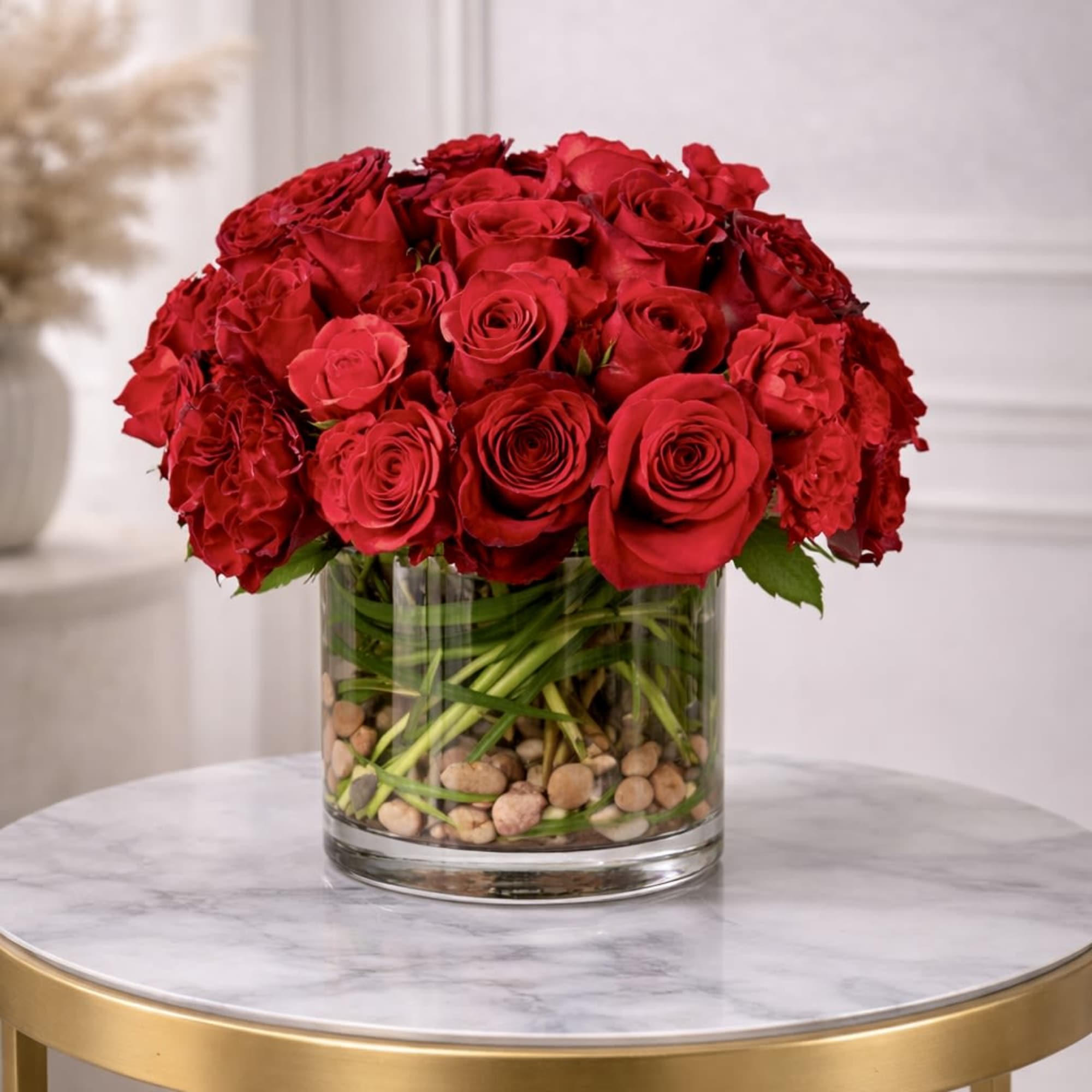 Low arrangement of red roses in a clear glass cylinder vase with stones on a small round table