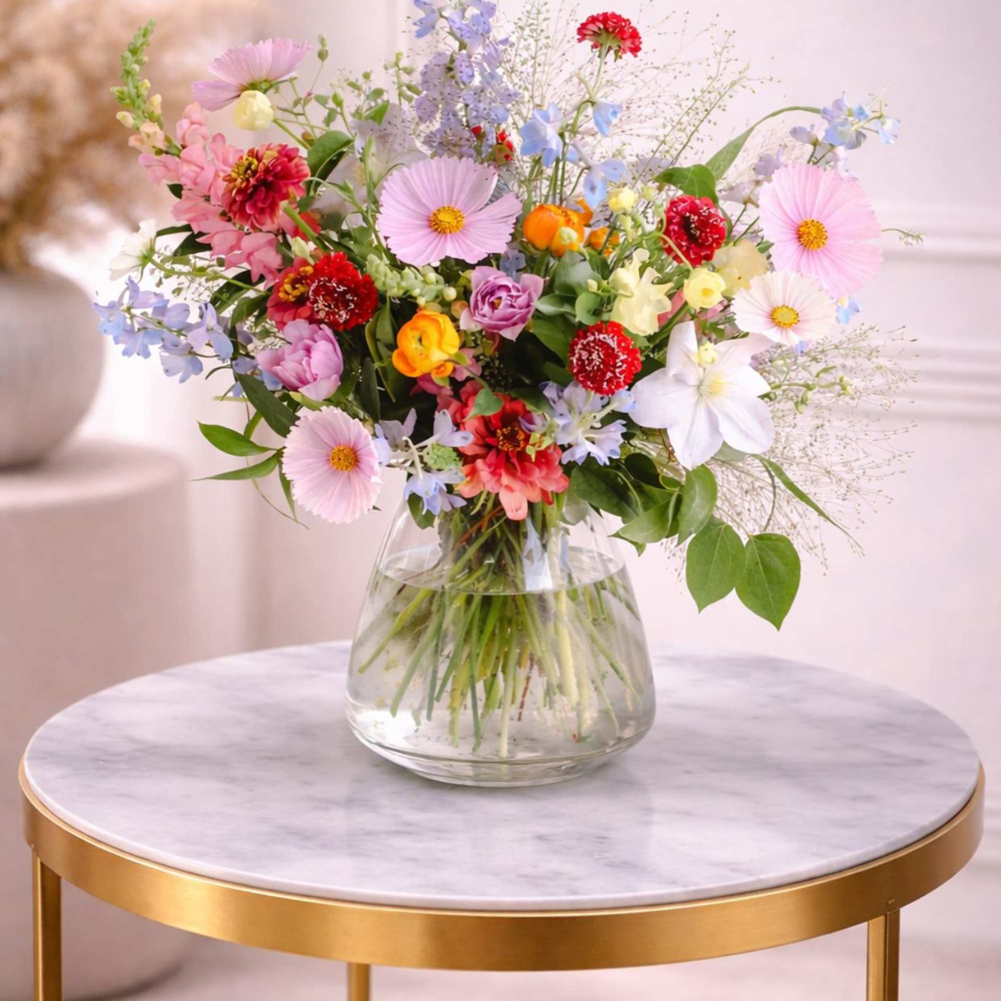 Colorful mixed spring flower arrangement in a clear glass vase on a marble-topped gold table