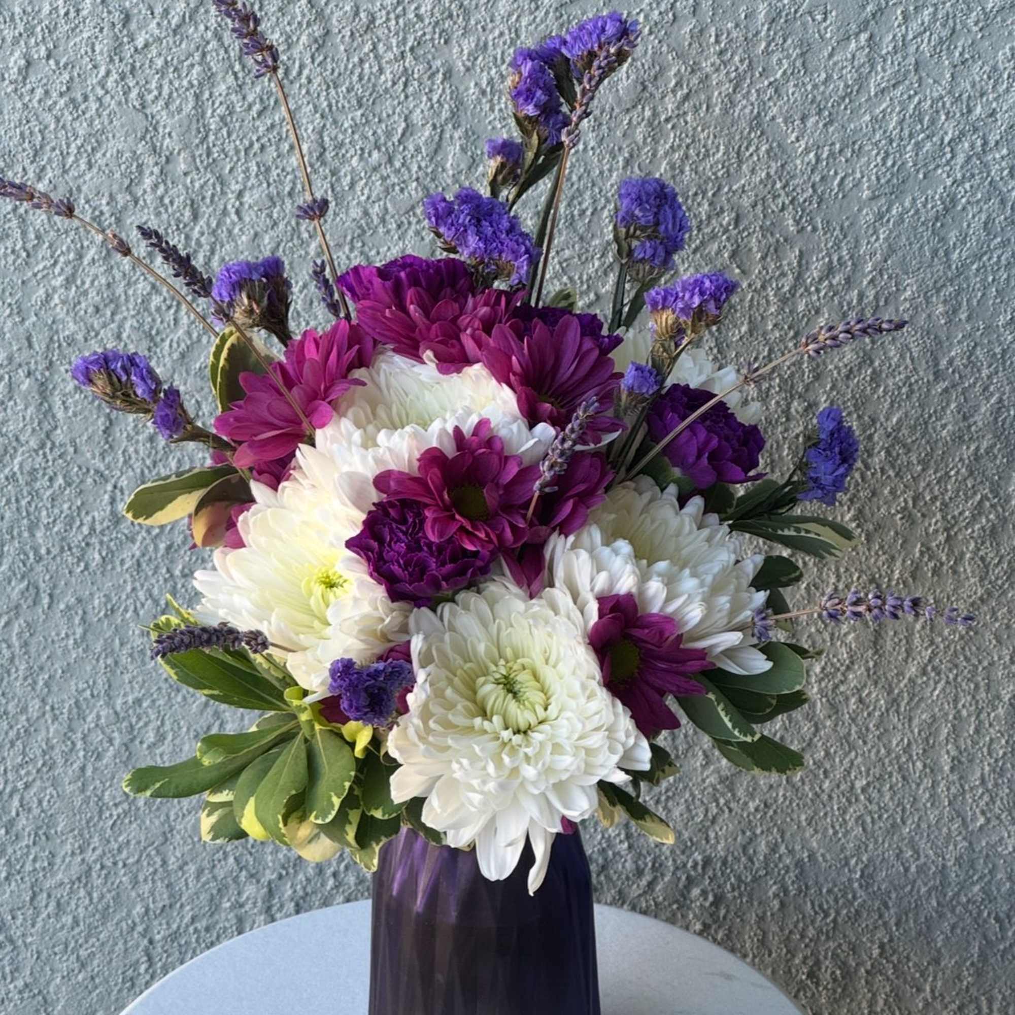 Purple and white chrysanthemum bouquet in a dark vase