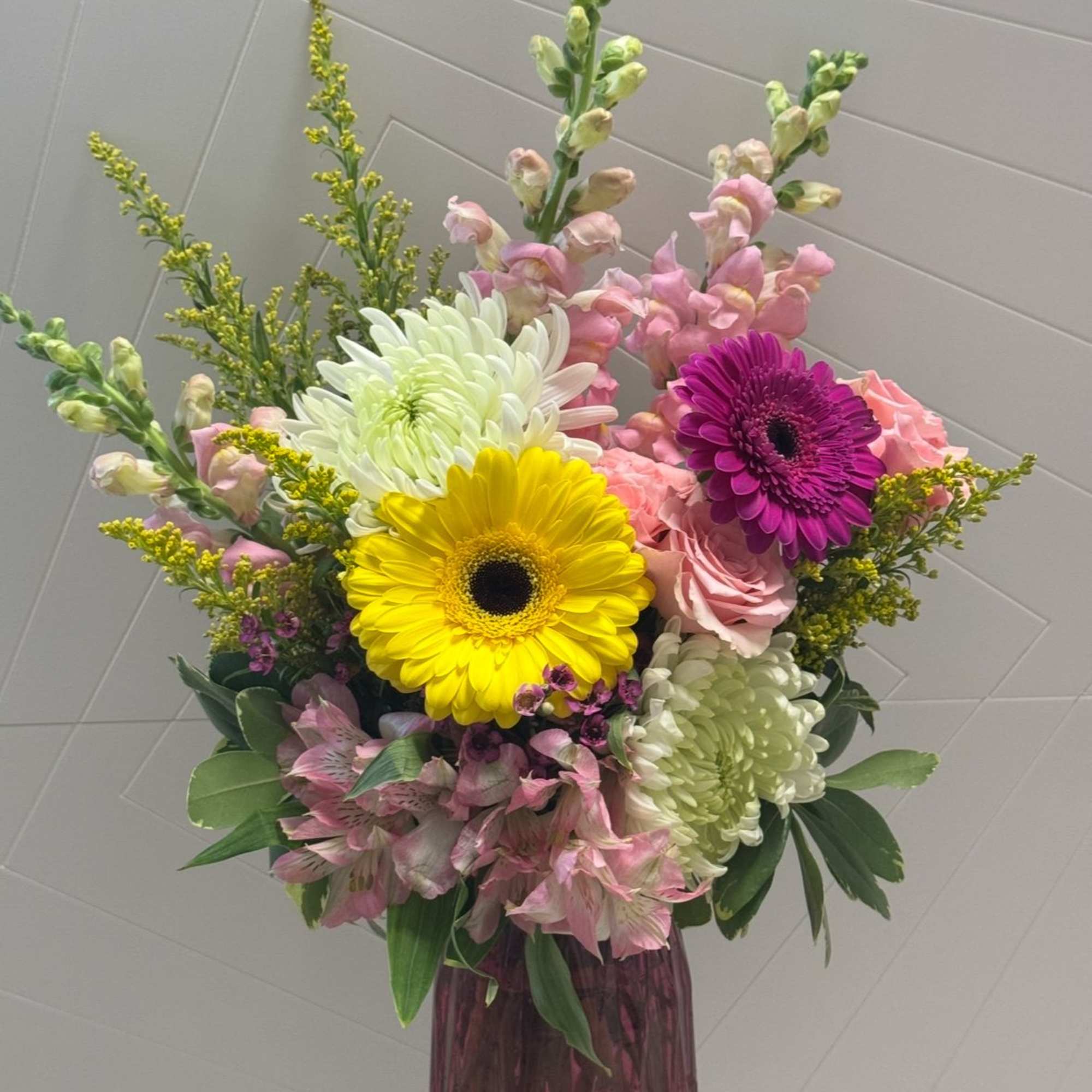 Mixed bouquet with gerbera daisies, roses, and snapdragons in a purple vase