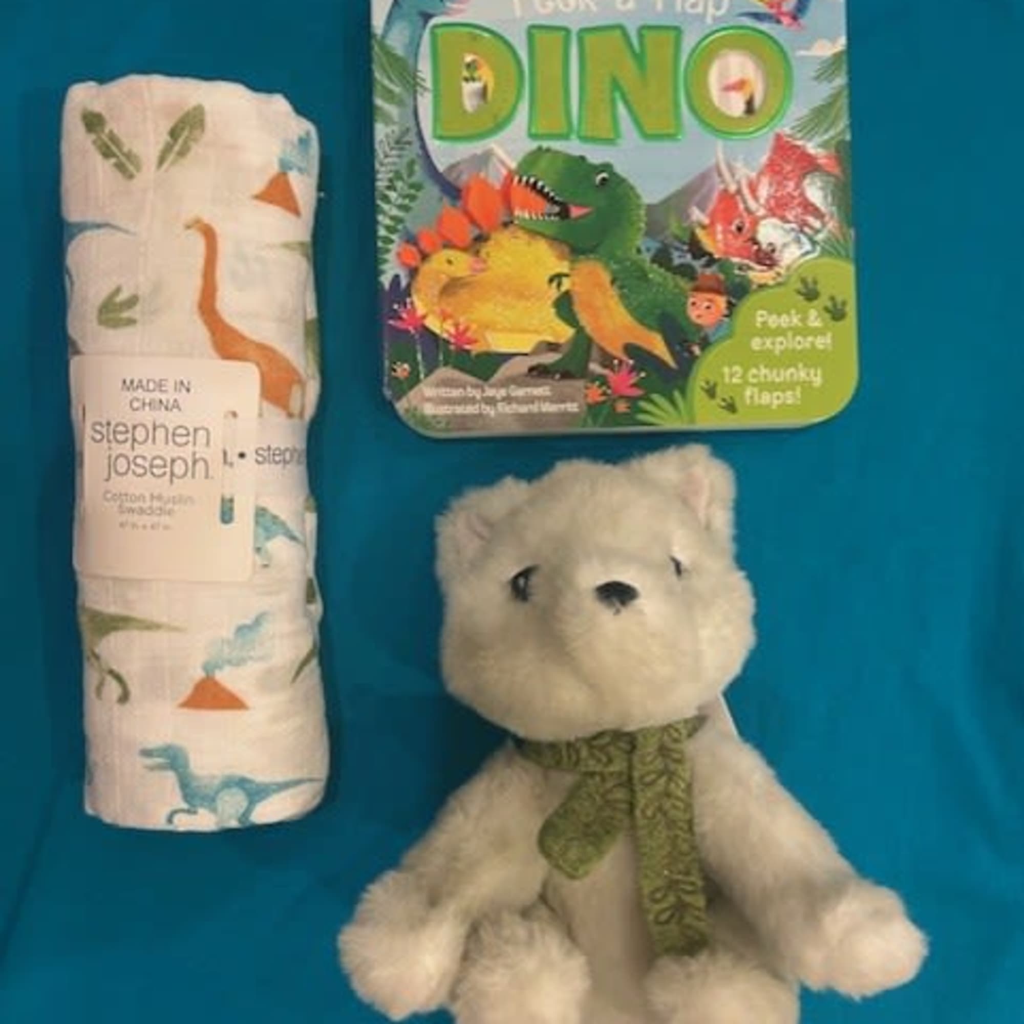 Baby gift set with a plush bear, dinosaur book, and rolled swaddle blanket