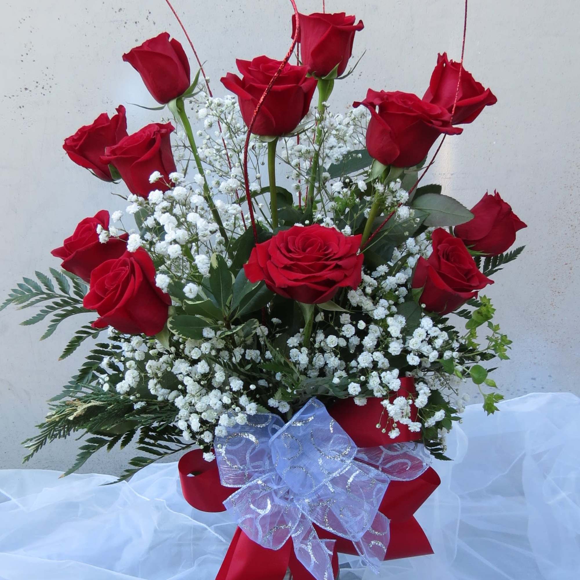 Red roses arranged in a clear glass vase with white baby's breath and a red ribbon bow