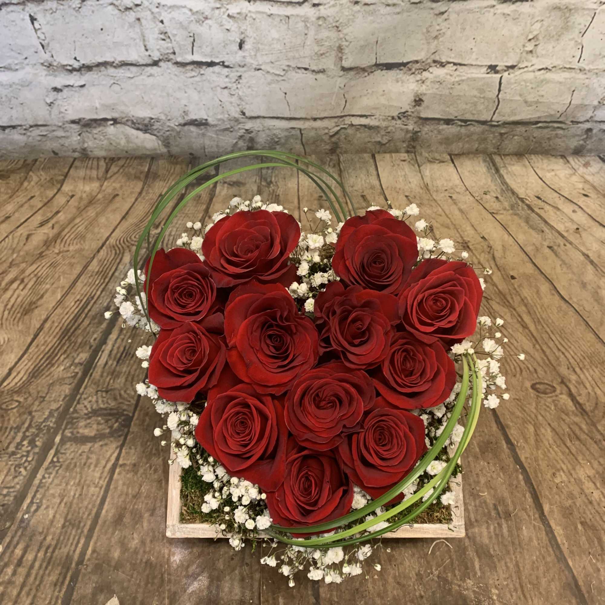 Heart-shaped arrangement of red roses with white baby's breath in a wooden box