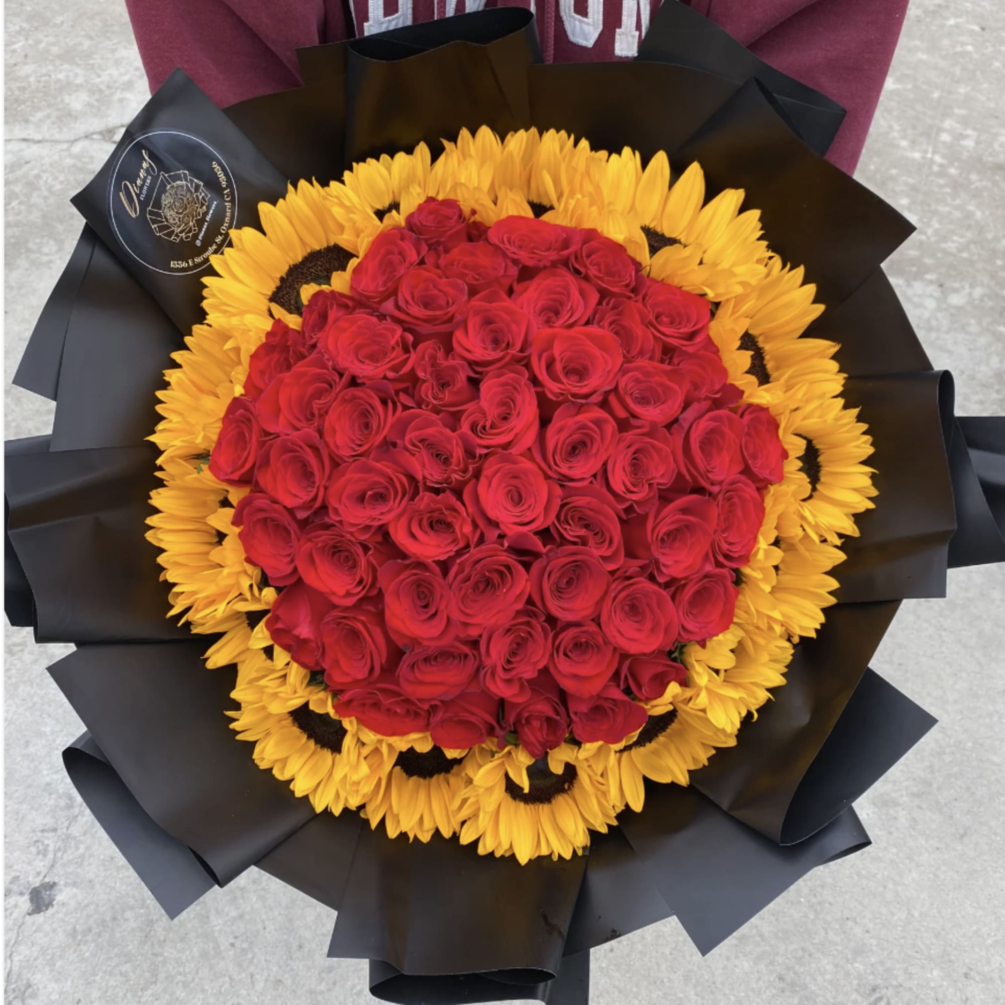 Red rose bouquet surrounded by yellow sunflowers in black wrap