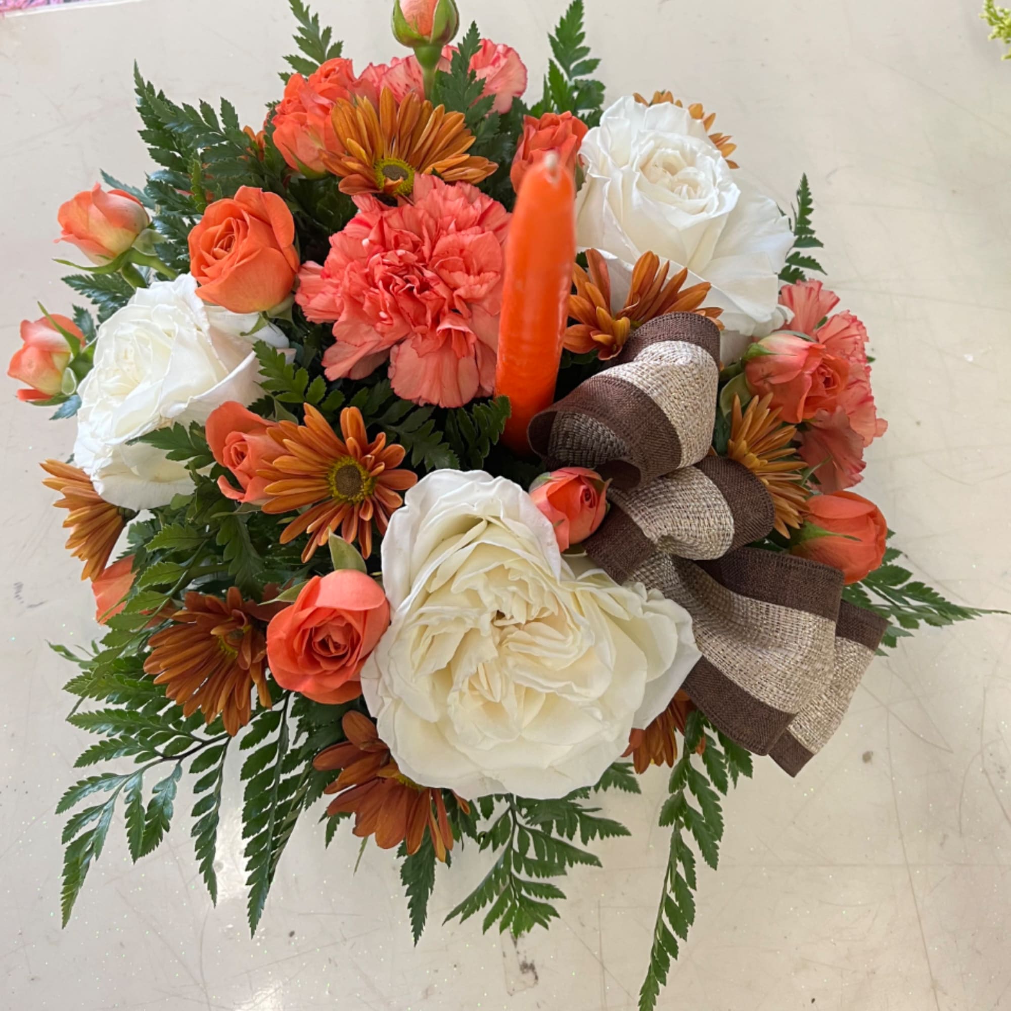 A compact fall centerpiece featuring white roses, orange carnations, and spray roses