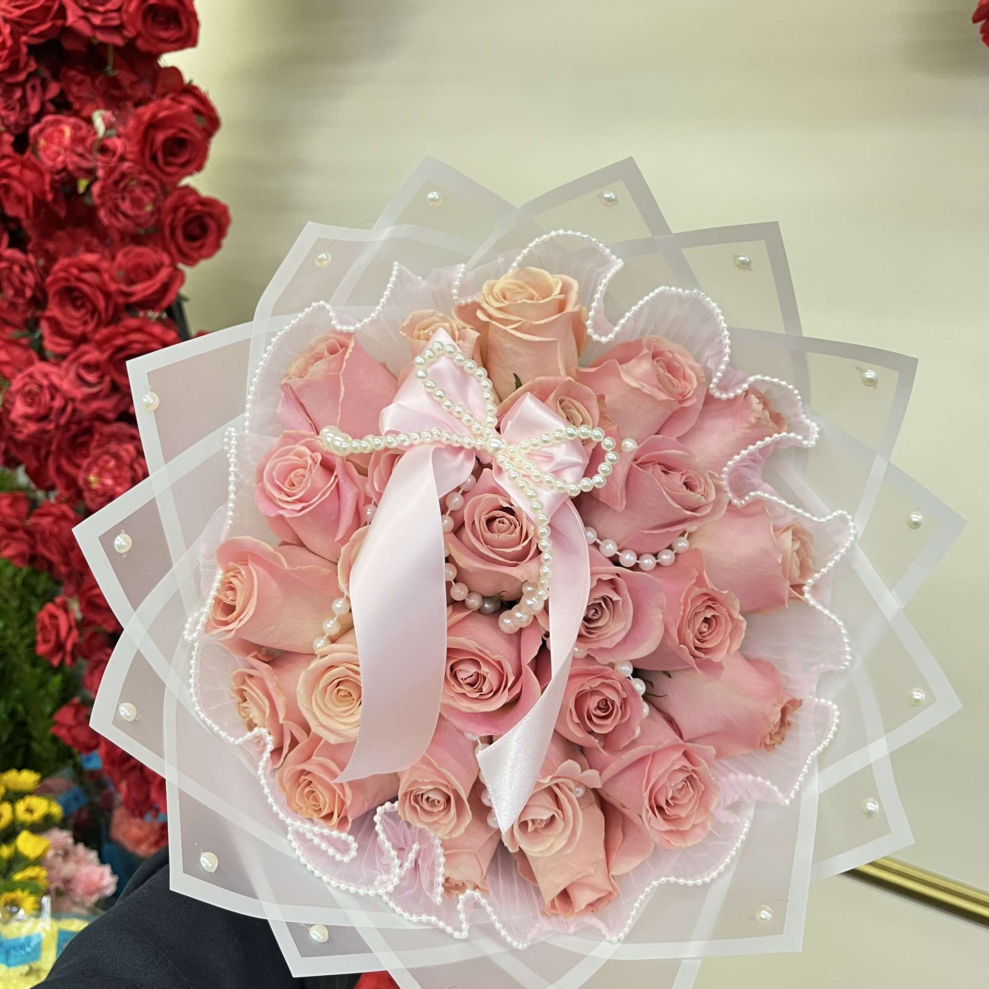Pink rose bouquet wrapped in sheer paper with a satin ribbon and pearl accents