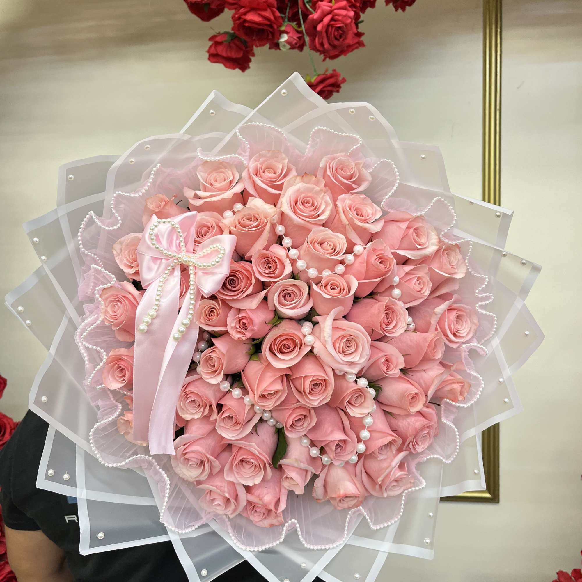 Large bouquet of pink roses wrapped in sheer white paper with a pink ribbon