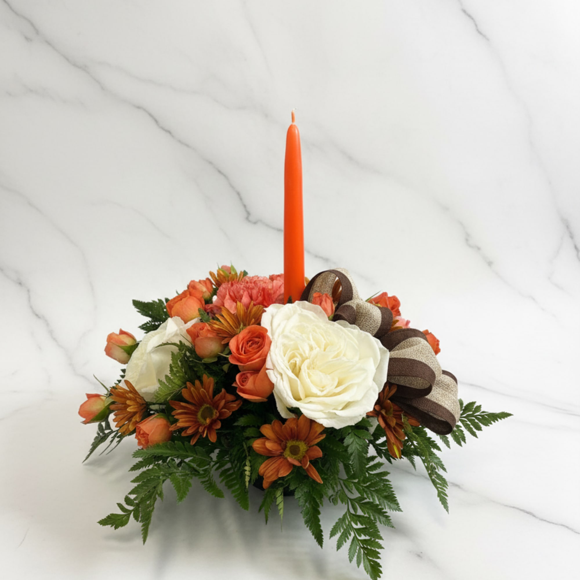 Orange floral centerpiece with a tall candle and ribbon bow
