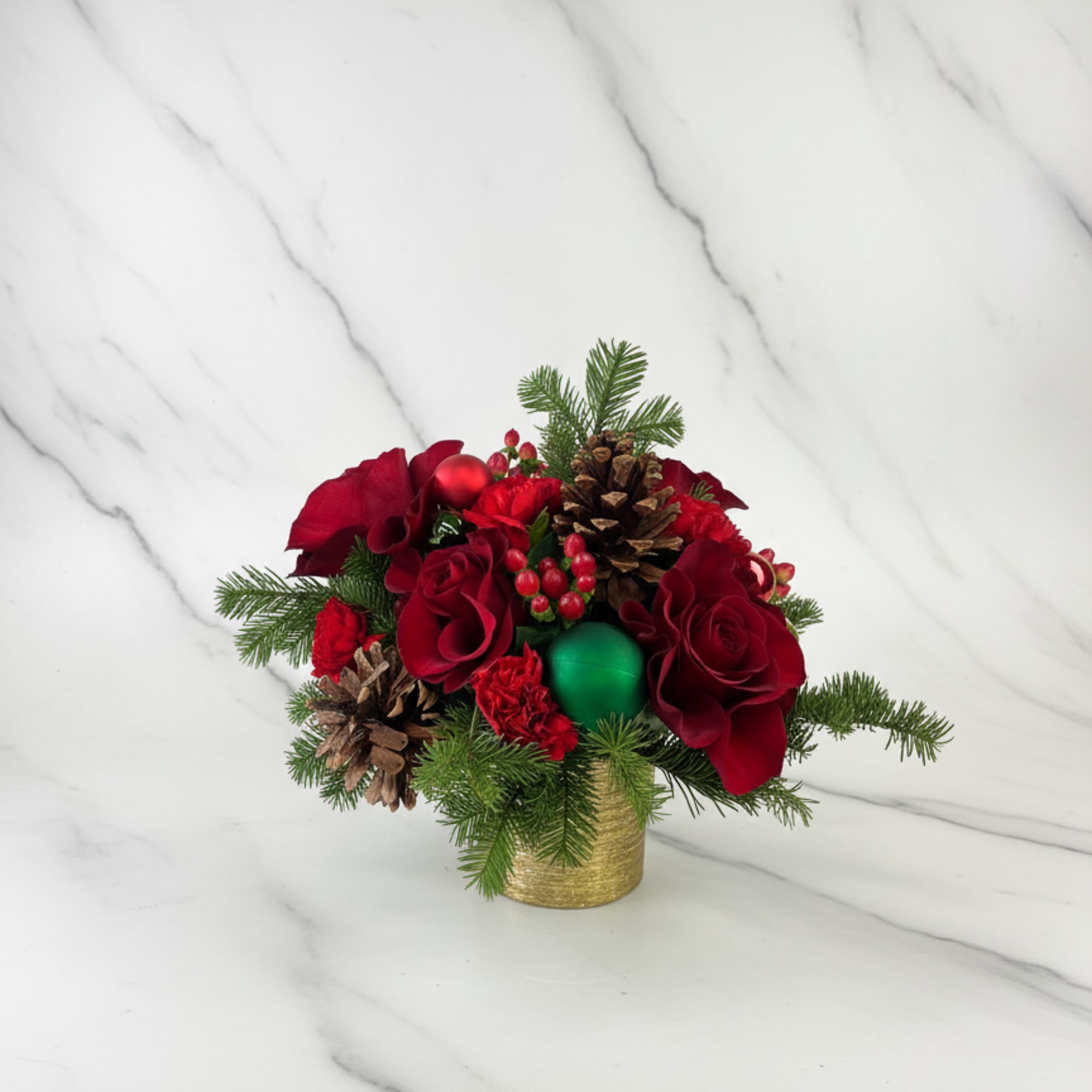 Red floral arrangement with pinecones and evergreen in a gold container
