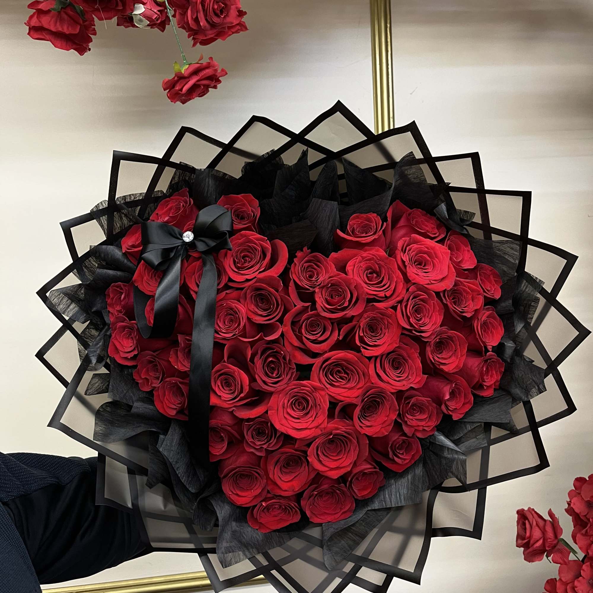 Heart-shaped bouquet of red roses wrapped in black paper with a black ribbon