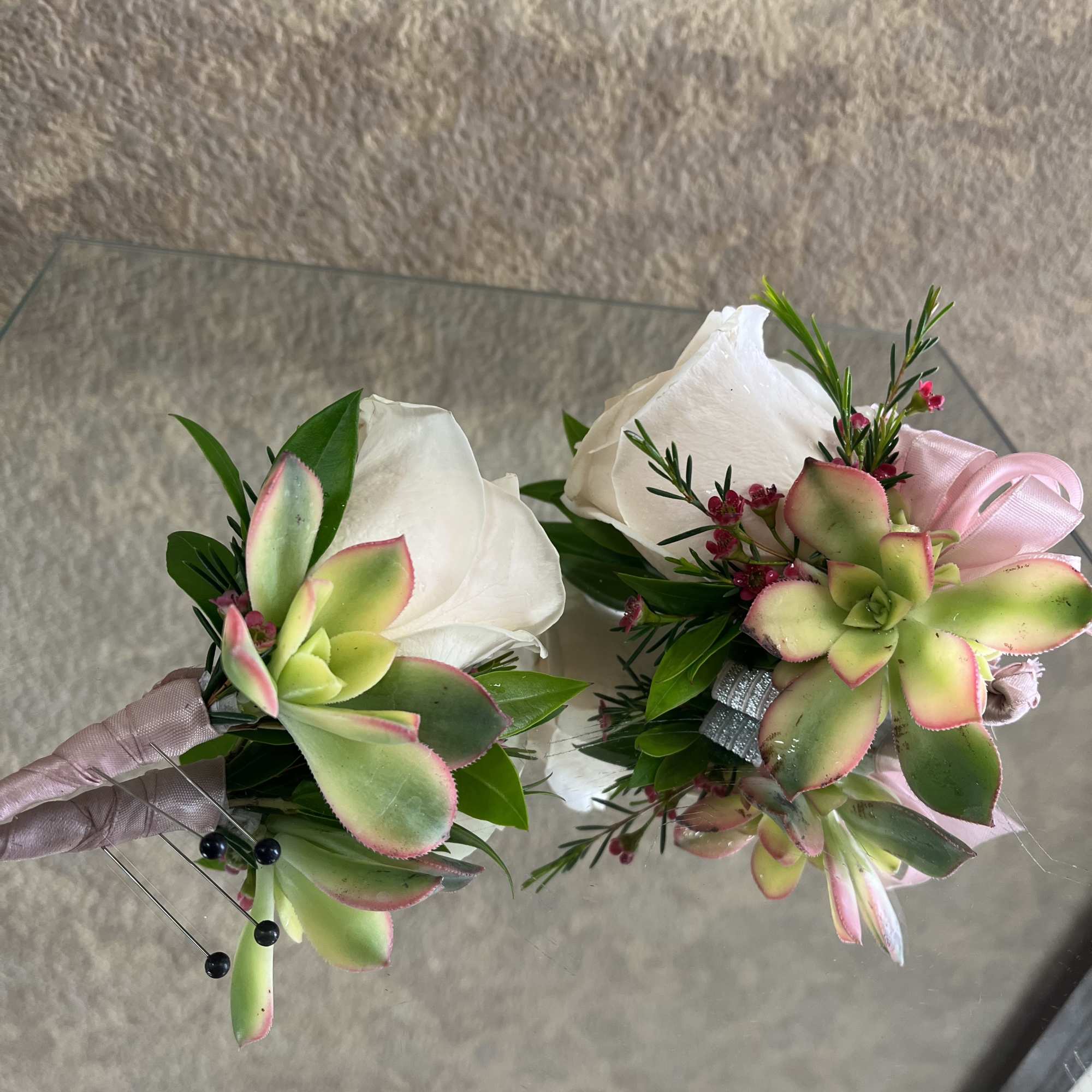Pair of white rose and succulent boutonnieres with pink accents on a mirrored surface