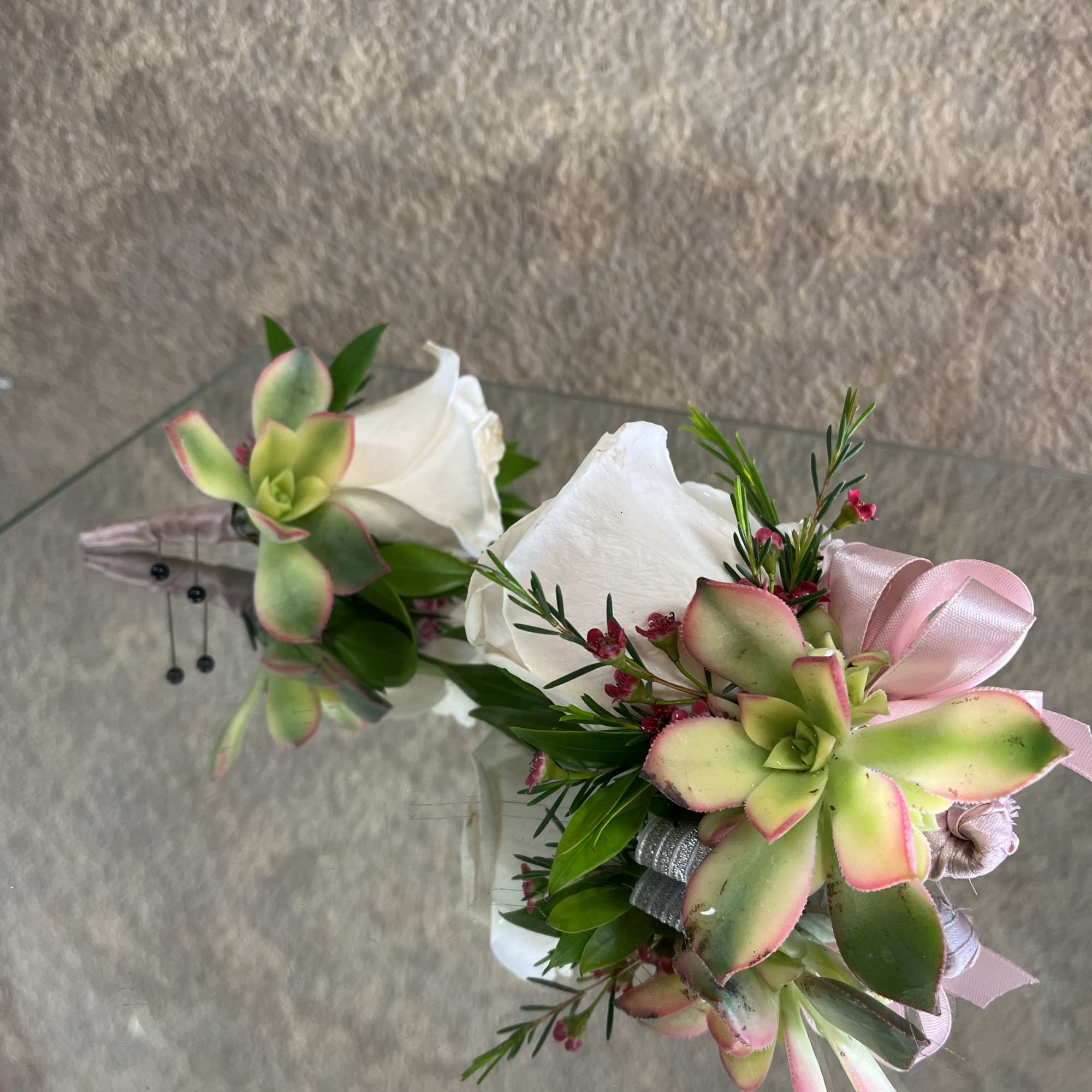 Two small succulent and white rose corsages with pink ribbon on a mirrored surface