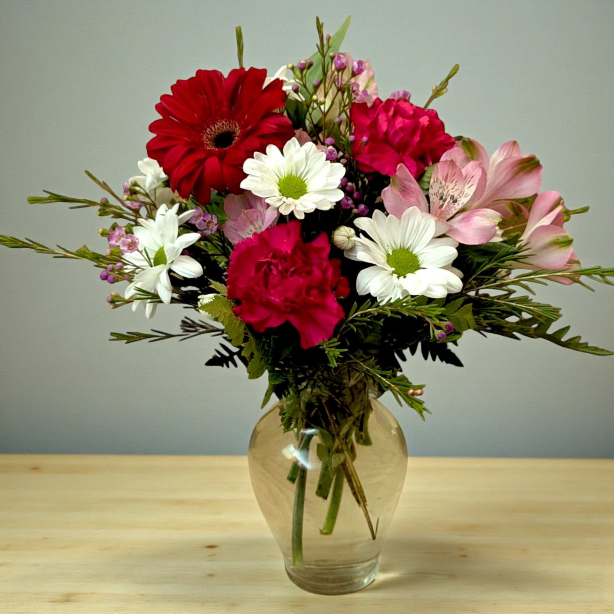 Mixed bouquet of red, pink, and white flowers in a clear glass vase