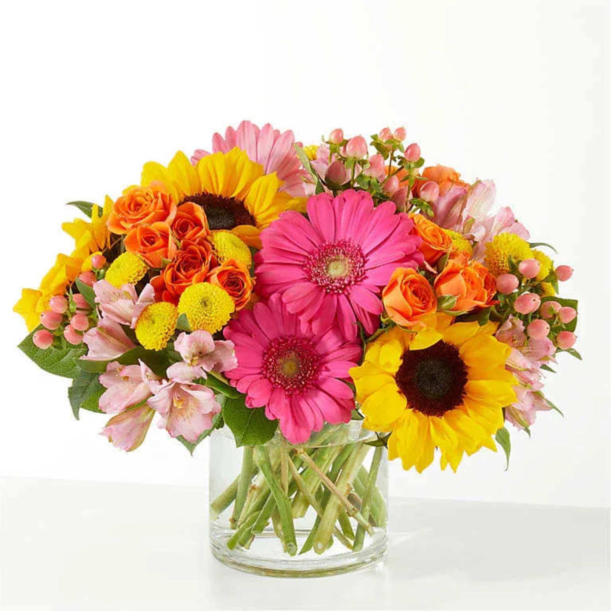 Bright mixed bouquet of sunflowers, gerbera daisies, and roses in a glass vase
