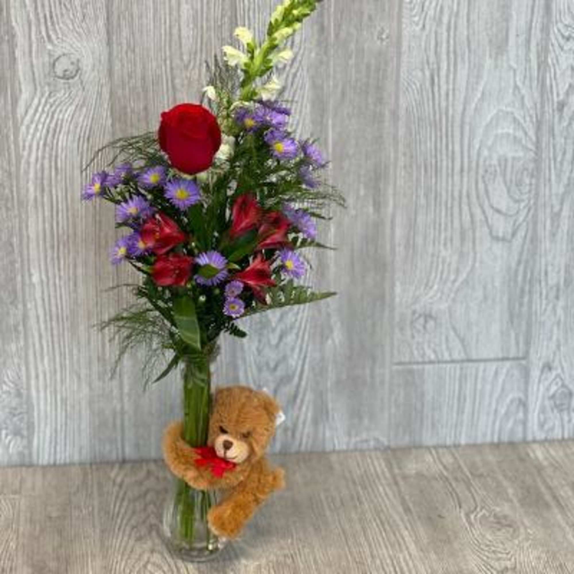 Bouquet of red and purple flowers in a glass vase with a teddy bear