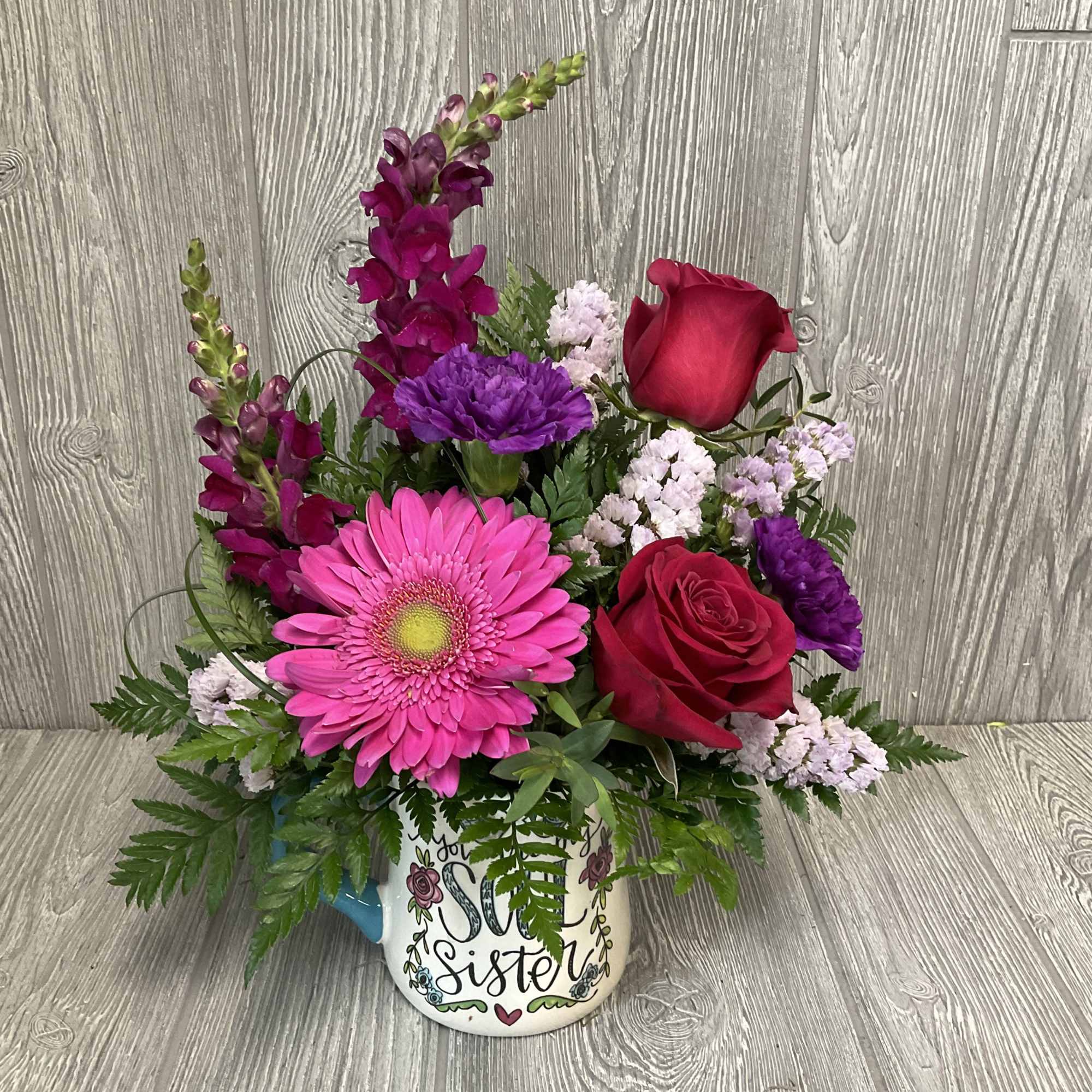 Pink and purple flower arrangement in a mug with "sister" text