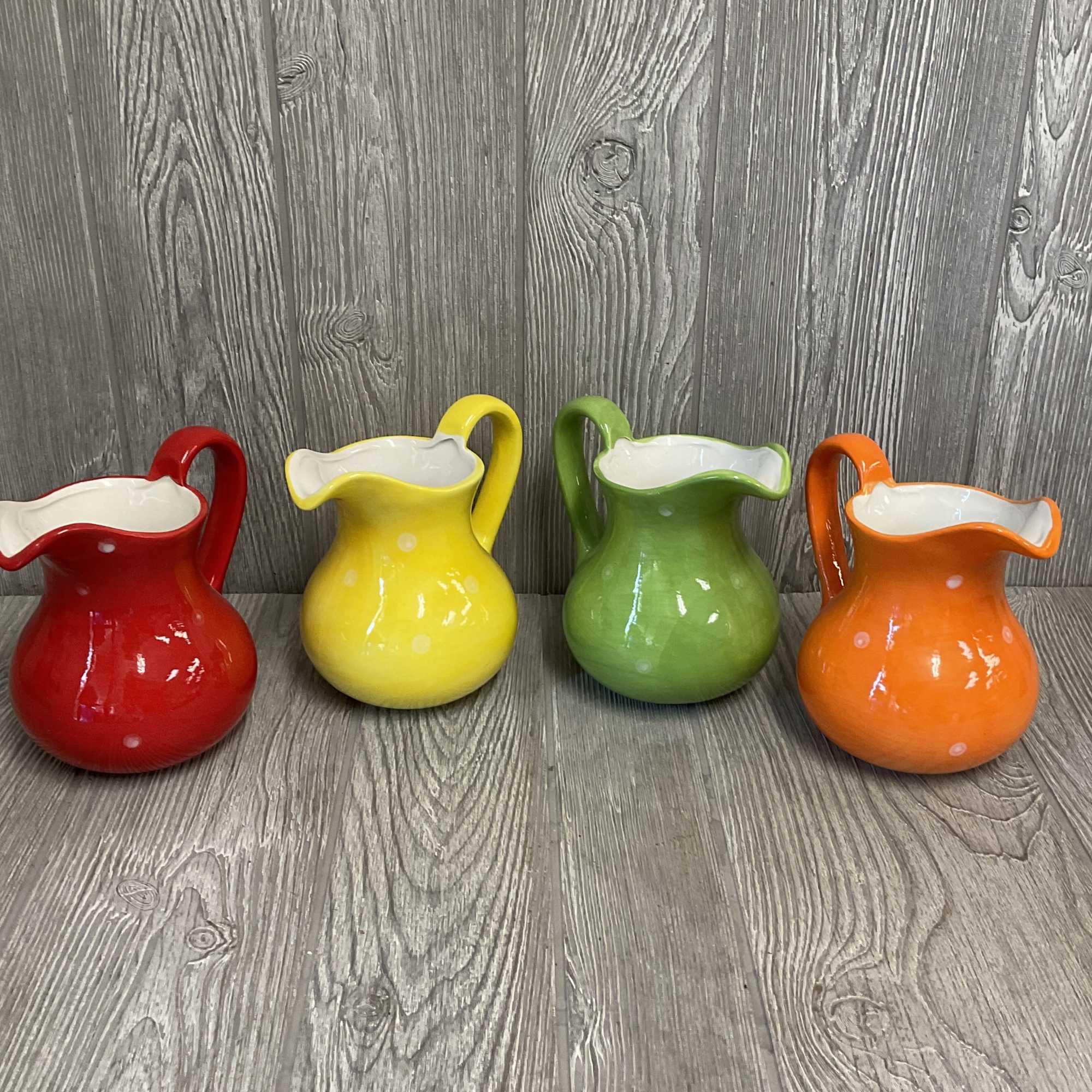 Four colorful ceramic pitchers with white interiors on a wood floor