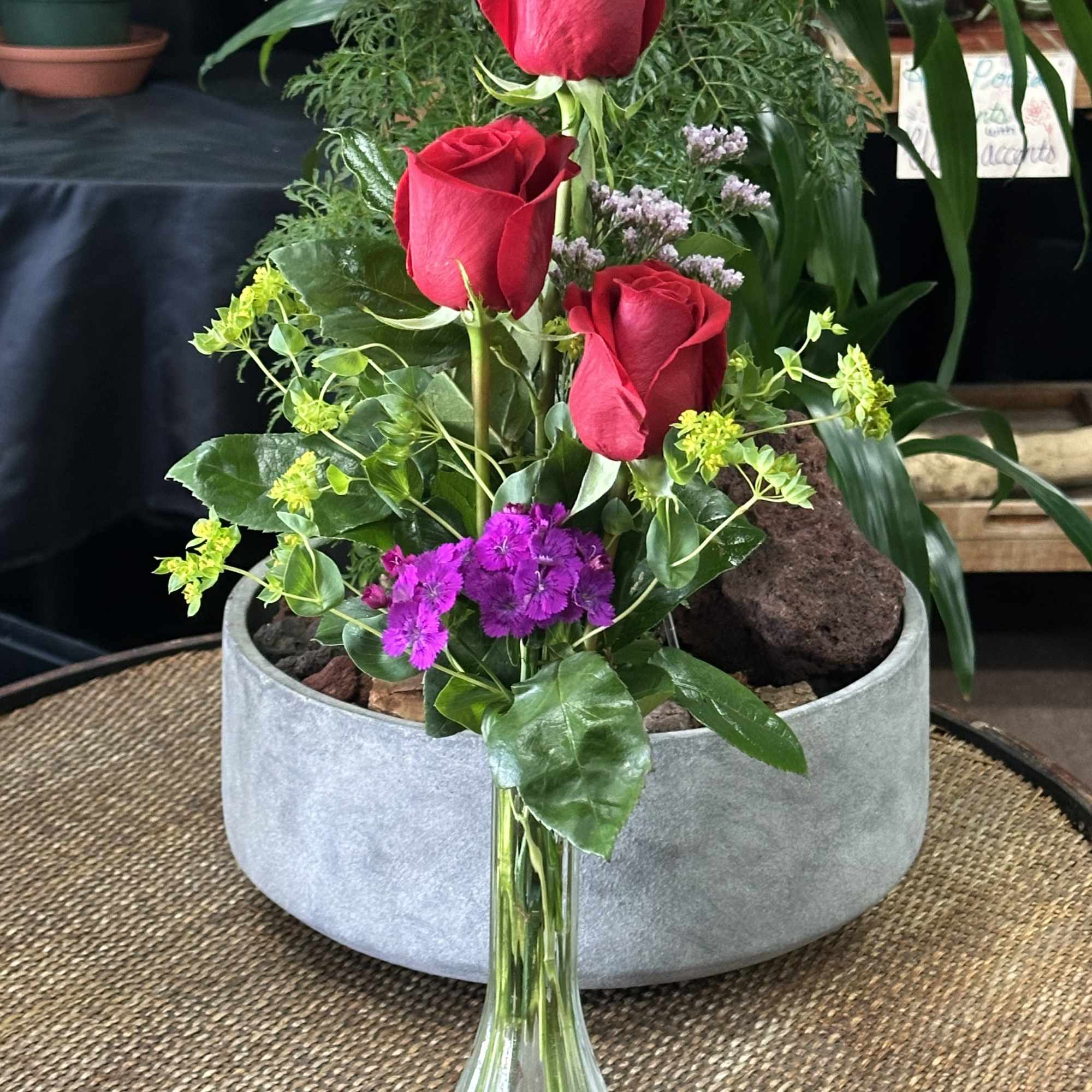 Three red roses in a clear glass vase with purple and yellow accents