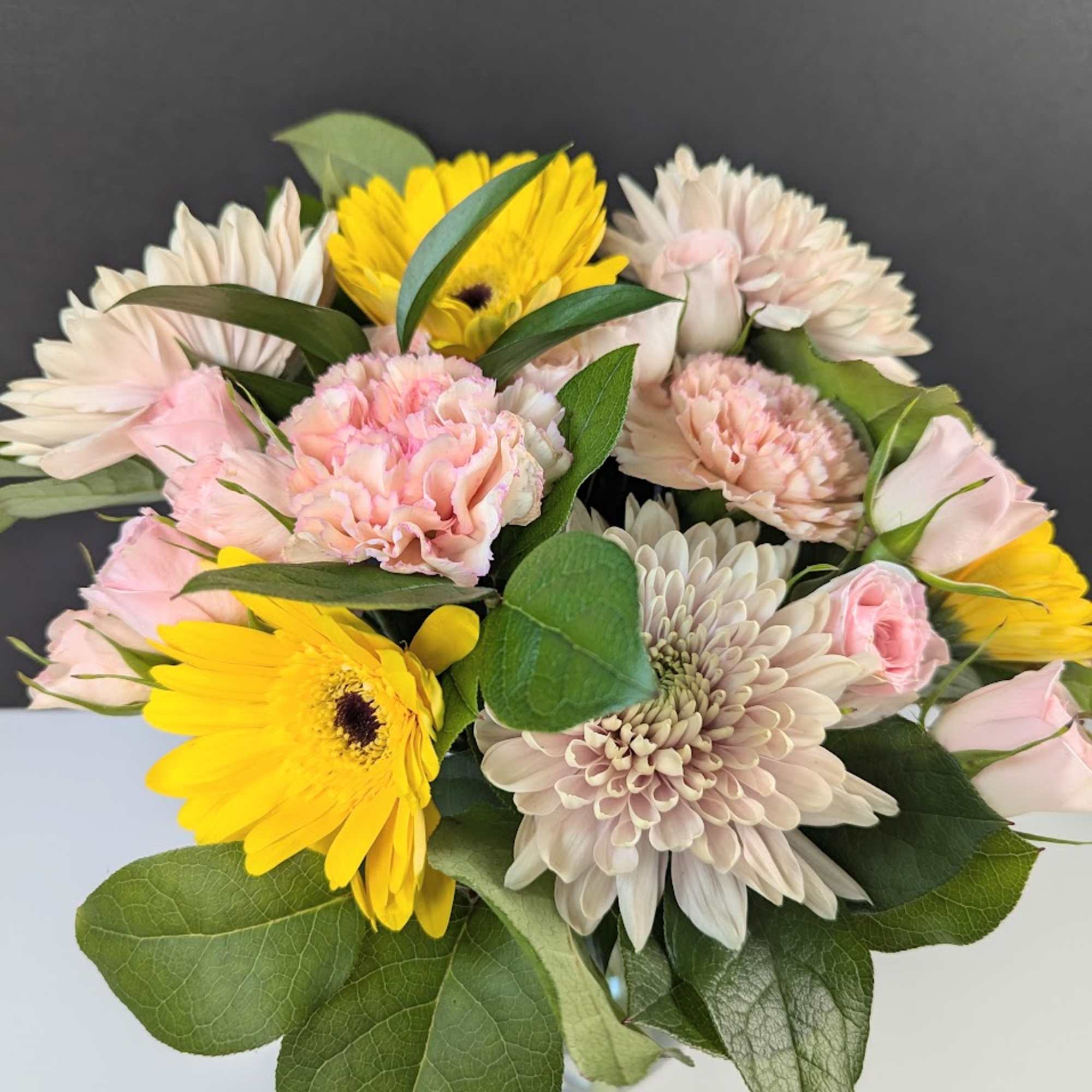 Bouquet of yellow gerbera daisies, pale pink carnations, and cream chrysanthemums