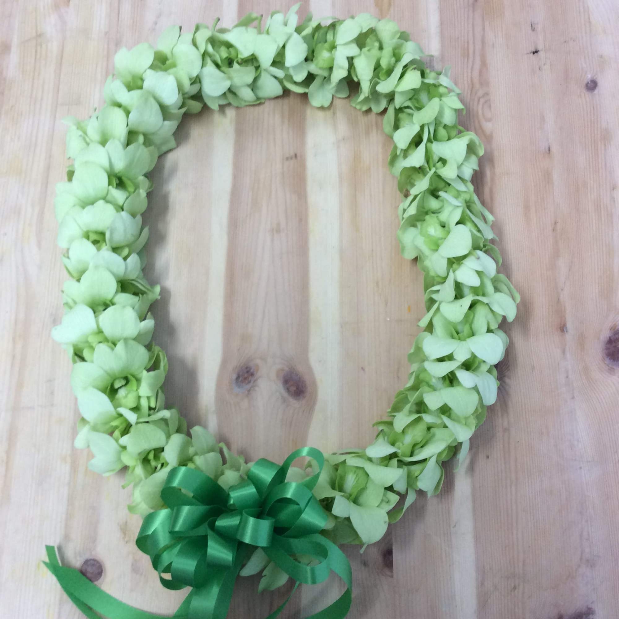 Green floral wreath with a ribbon bow on a wooden surface