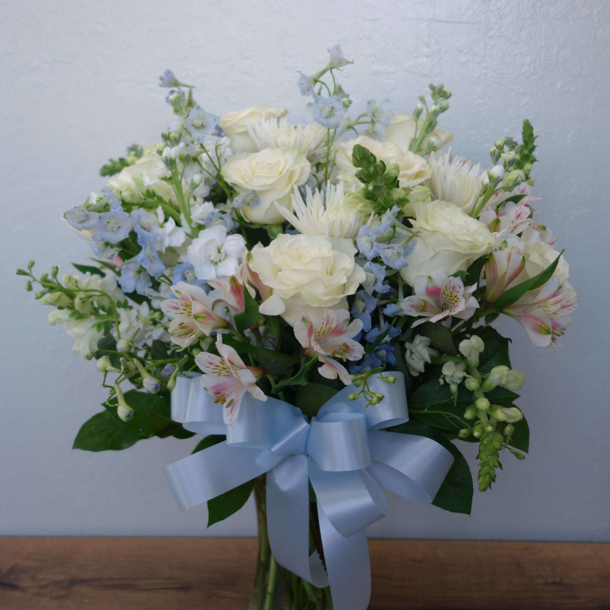 White and pale blue mixed bouquet in a glass vase with a blue ribbon