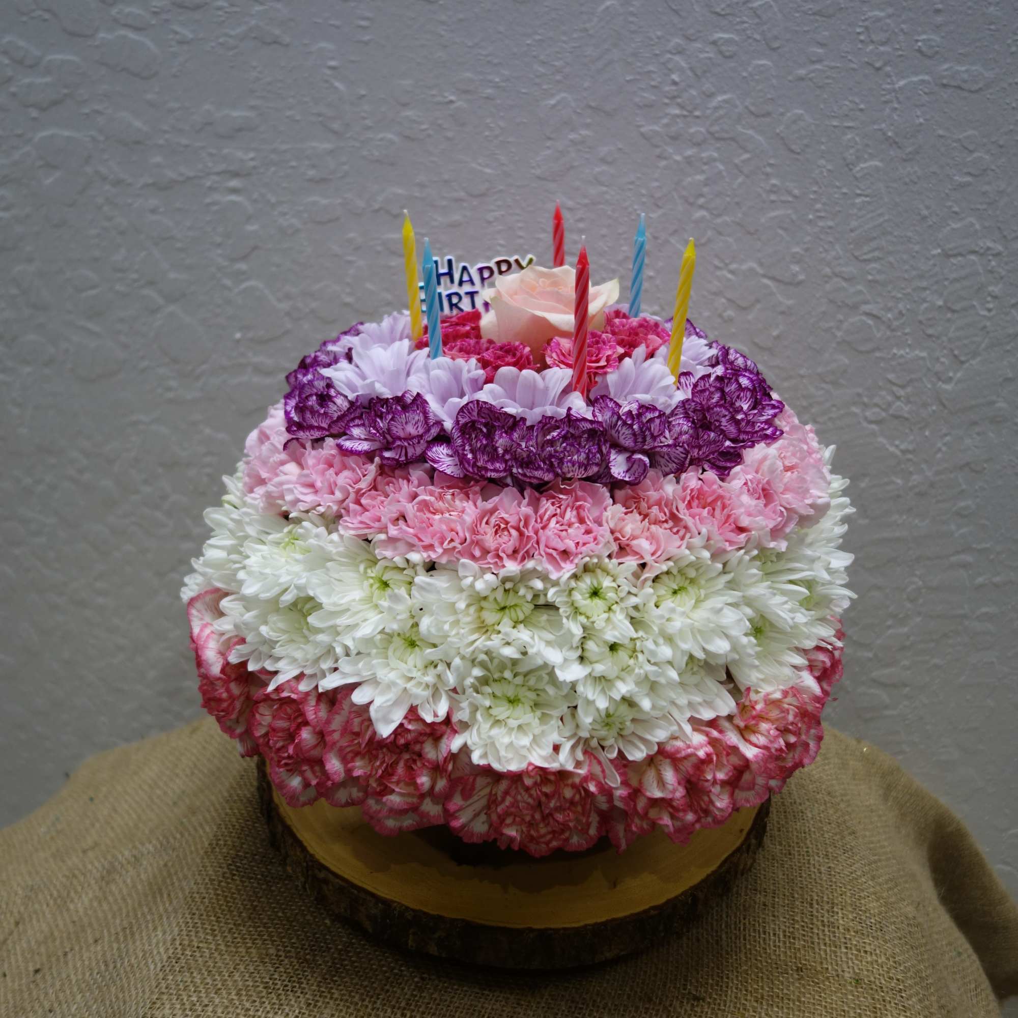 Round flower-covered birthday cake with candles and a rose topper