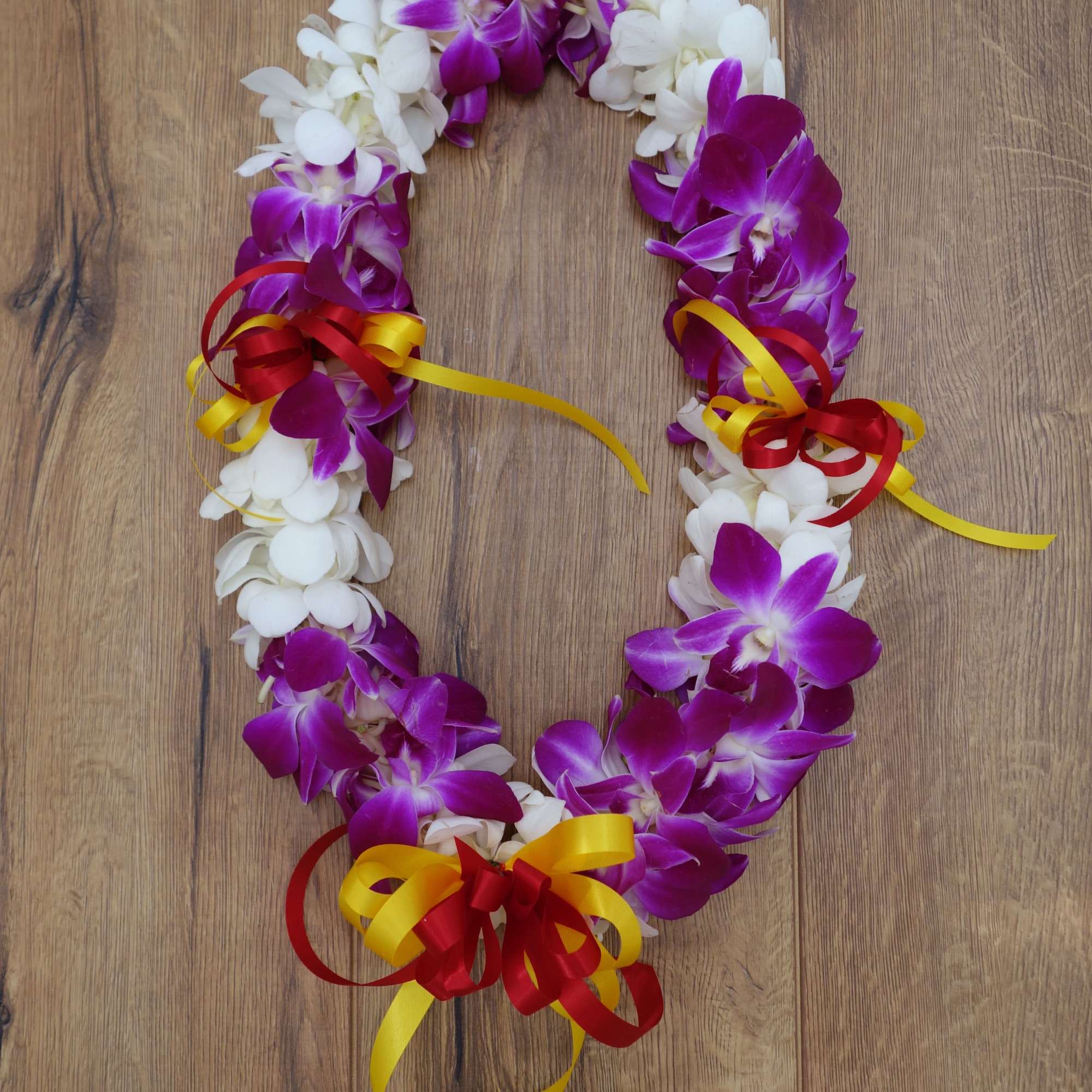 Purple and white orchid lei with red and yellow ribbons