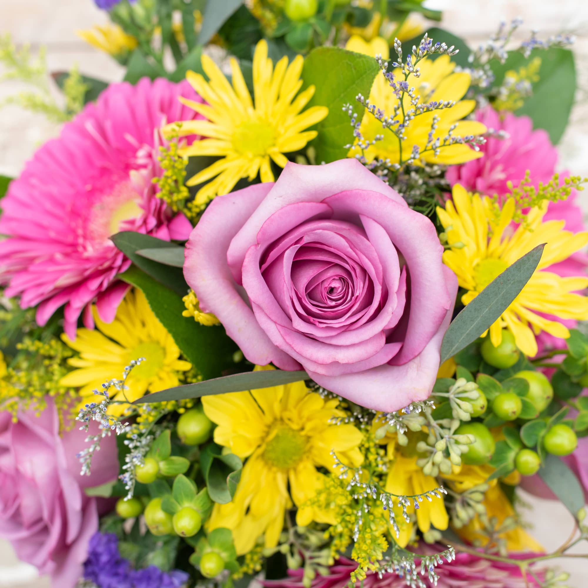 Pink rose surrounded by yellow daisies in a mixed bouquet