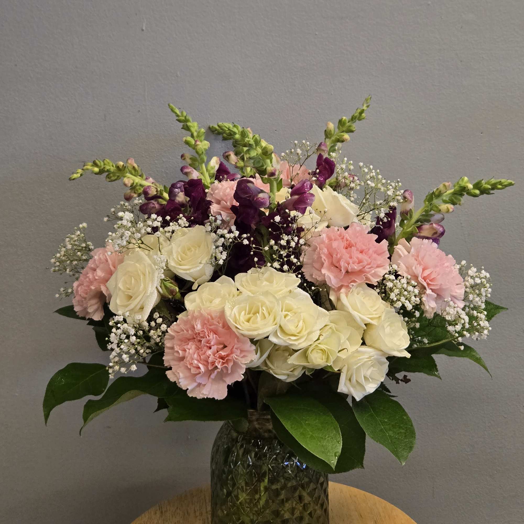 This arrangement includes cream roses, pink carnations, purple snapdragons, and delicate white