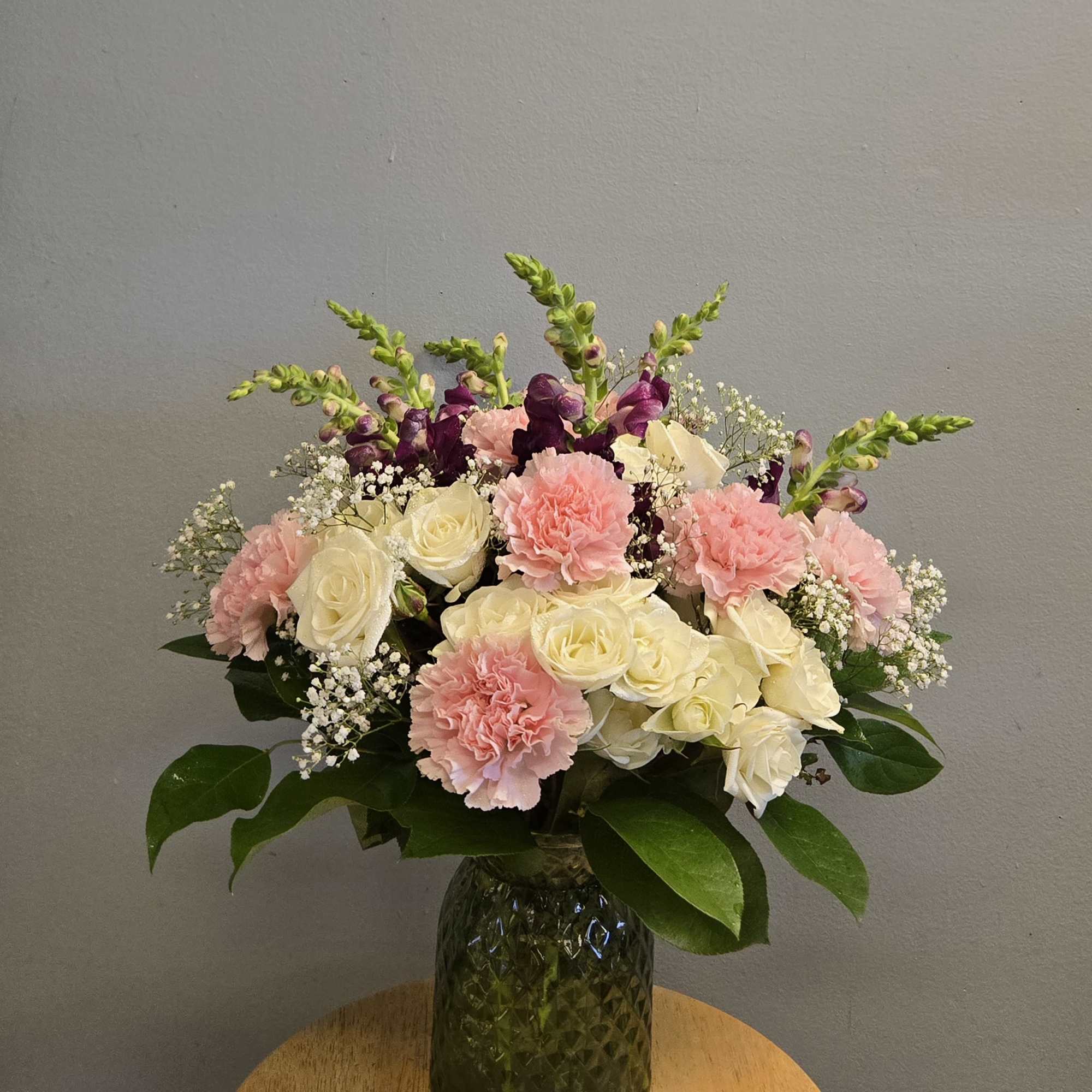 This arrangement includes cream roses, pink carnations, purple snapdragons, and delicate white