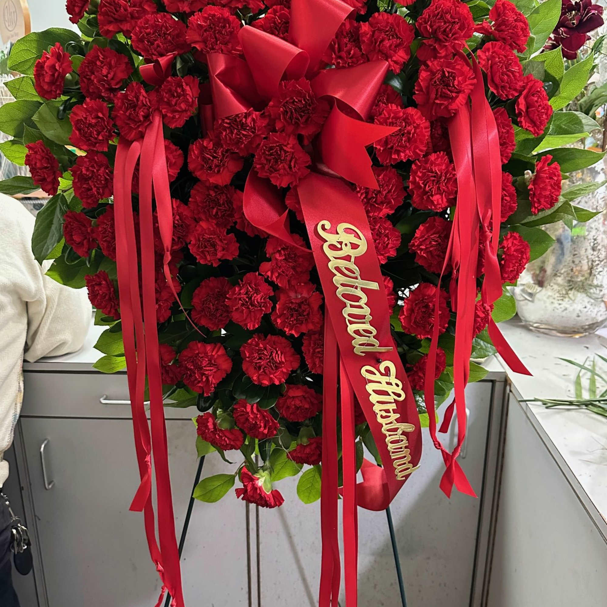 Heart-shaped standing spray of red carnations with ribbon
