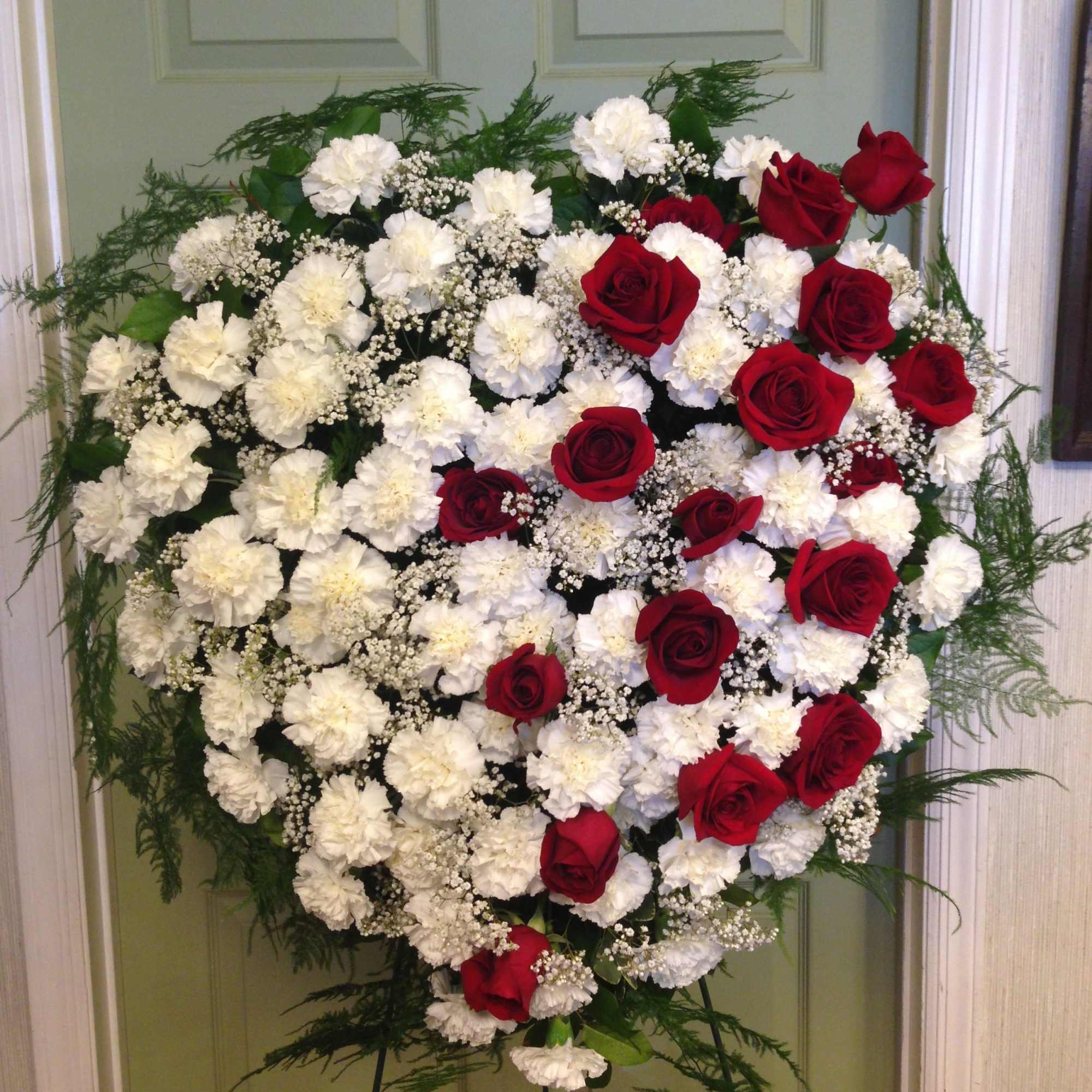 Heart-shaped floral spray of red roses and white carnations on an easel