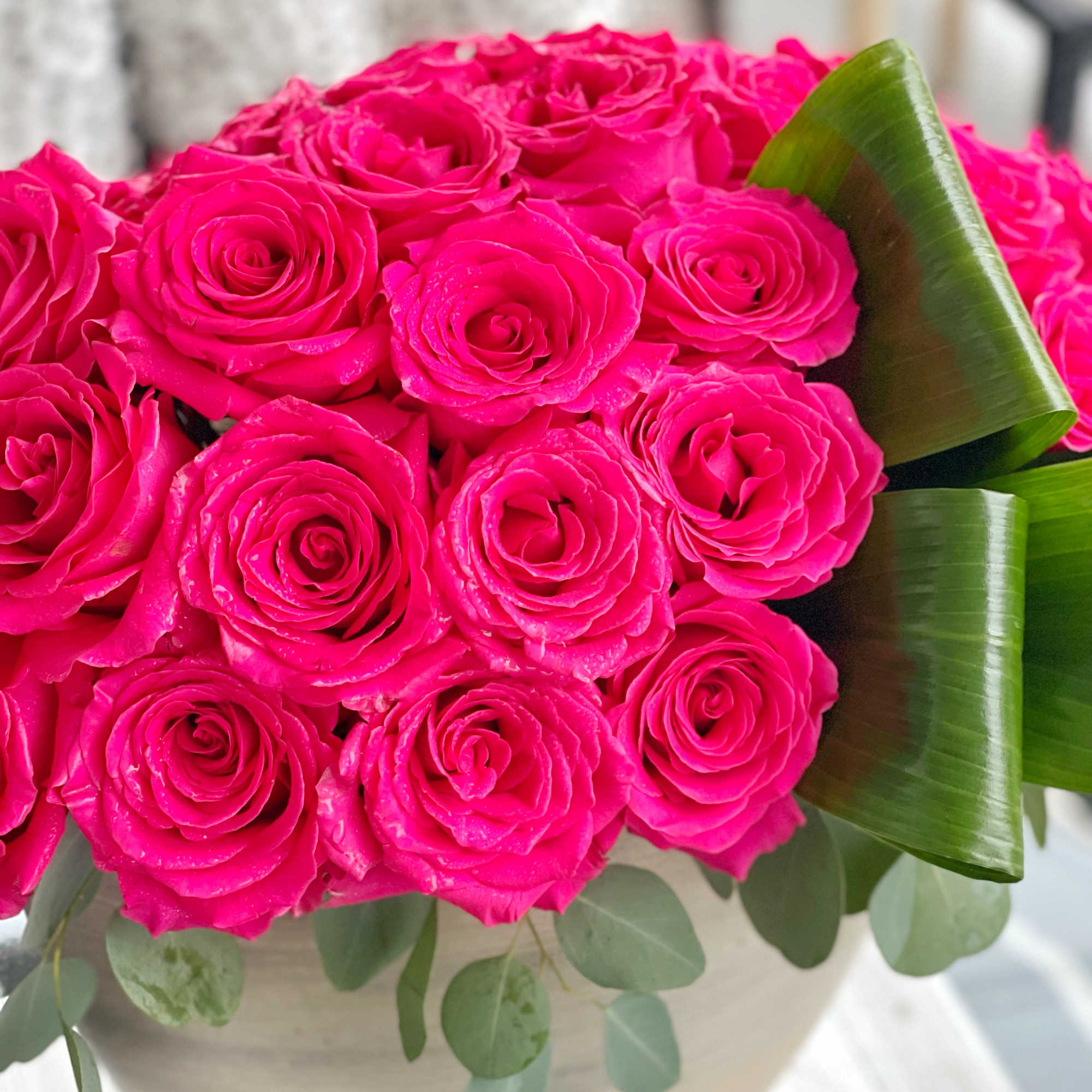 Bright pink rose bouquet in a cream vase with green leaves