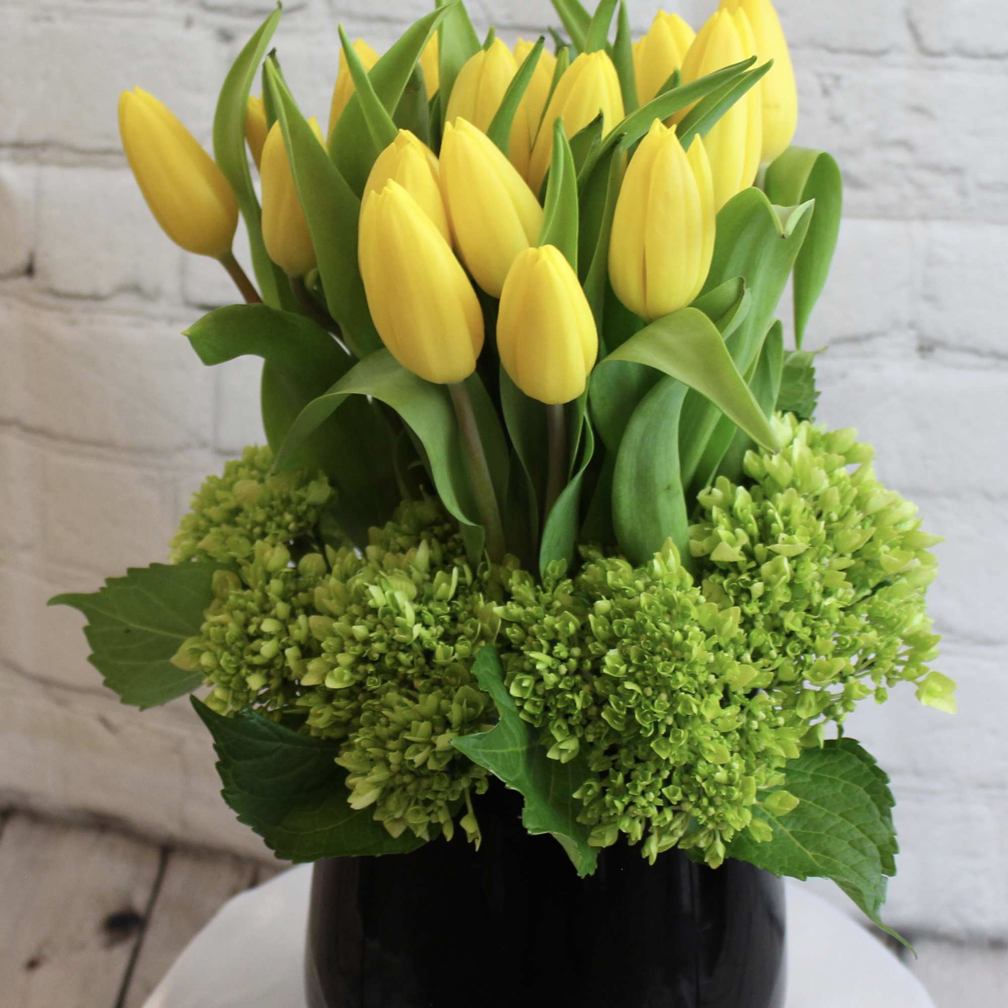 Yellow tulips arranged in a black vase with green hydrangeas