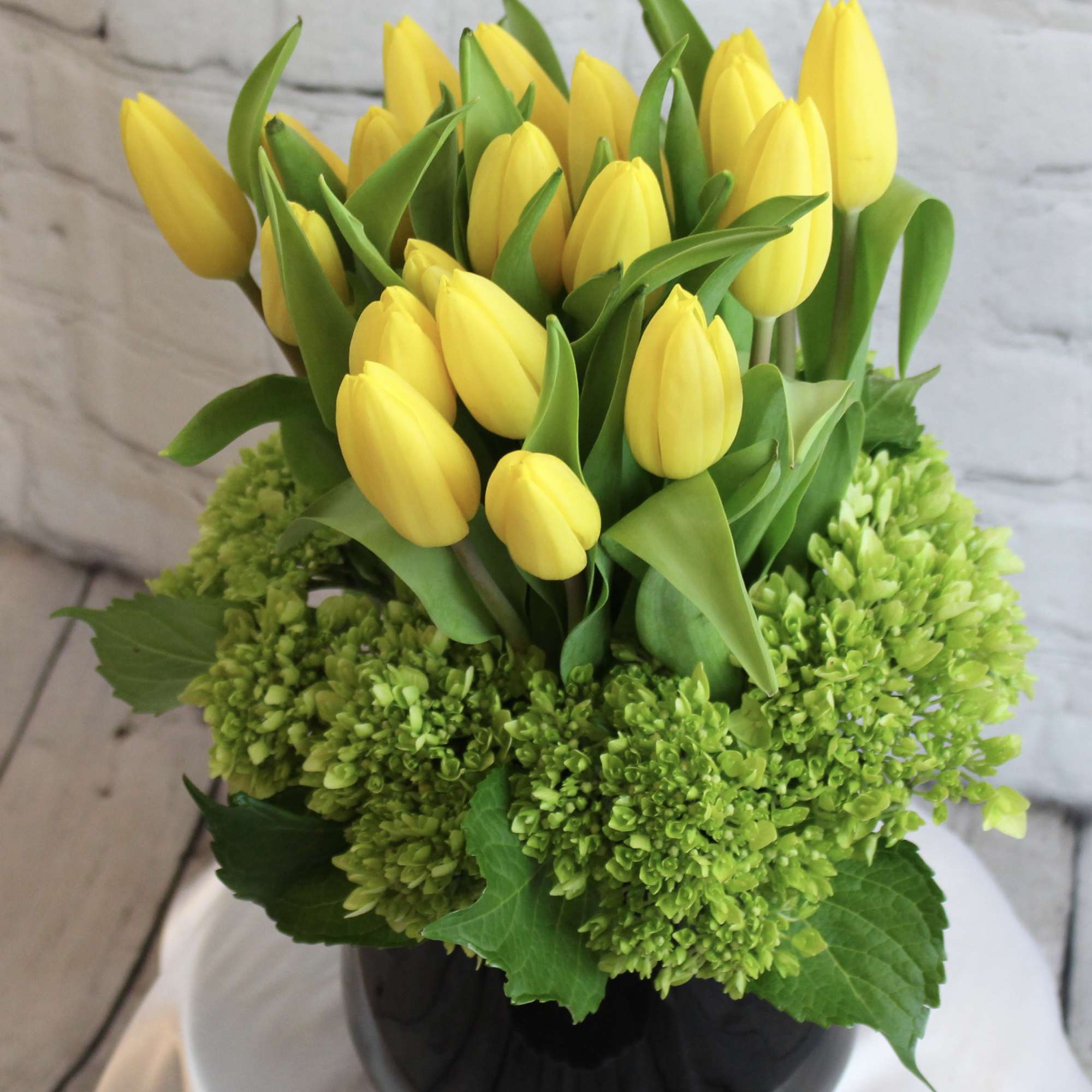 Yellow tulips arranged in a black vase with green hydrangeas