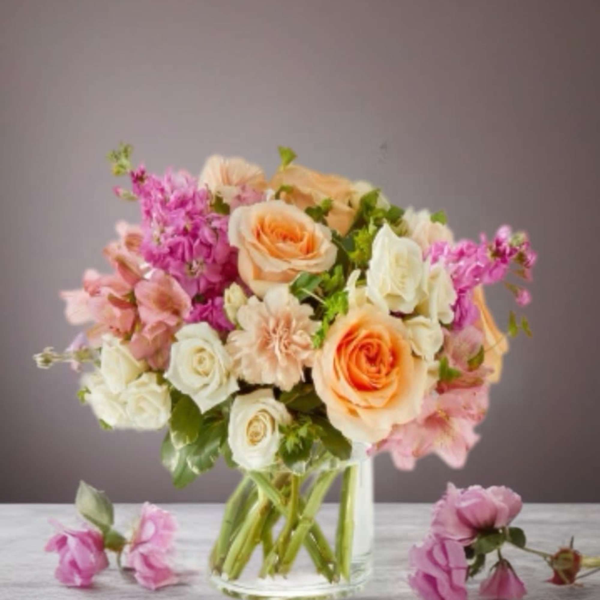 Bouquet of peach and white roses with pink flowers in a clear glass vase