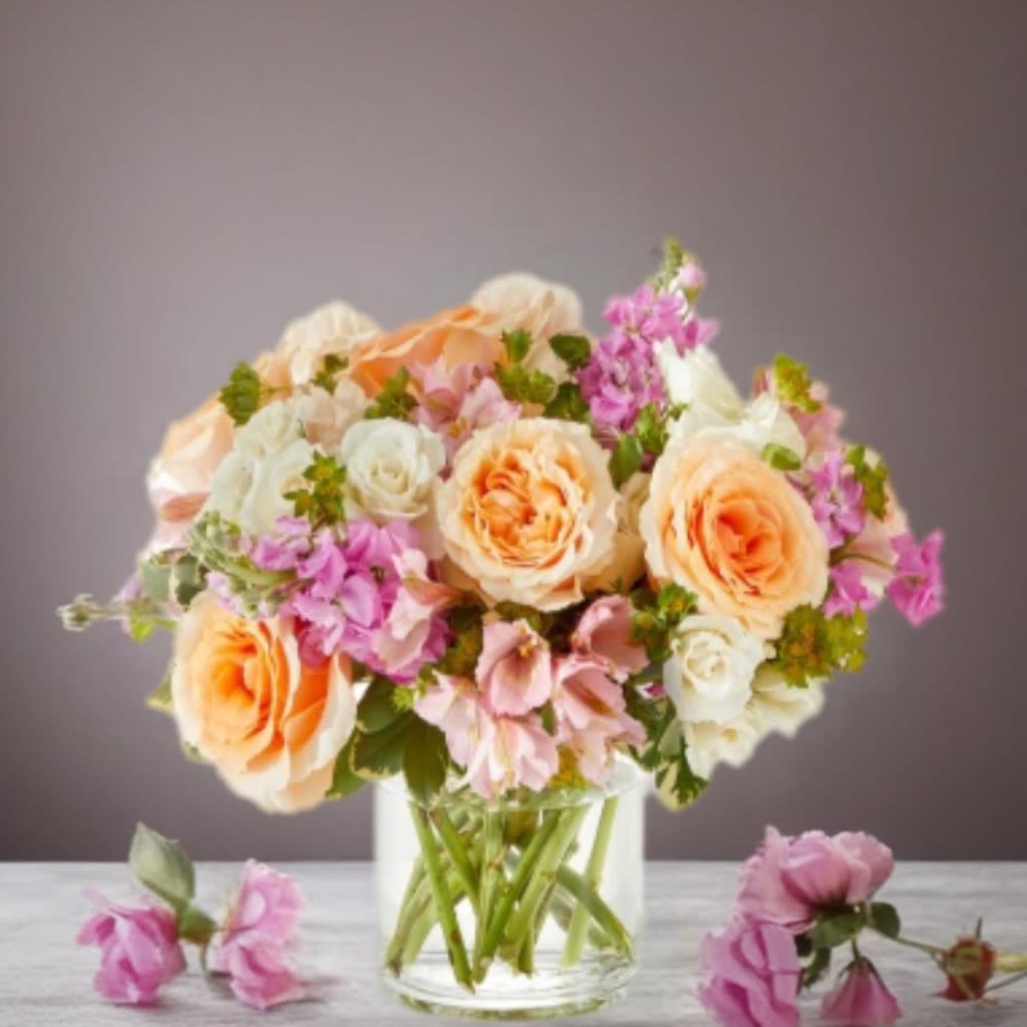 Peach and white roses with pink flowers in a clear glass vase