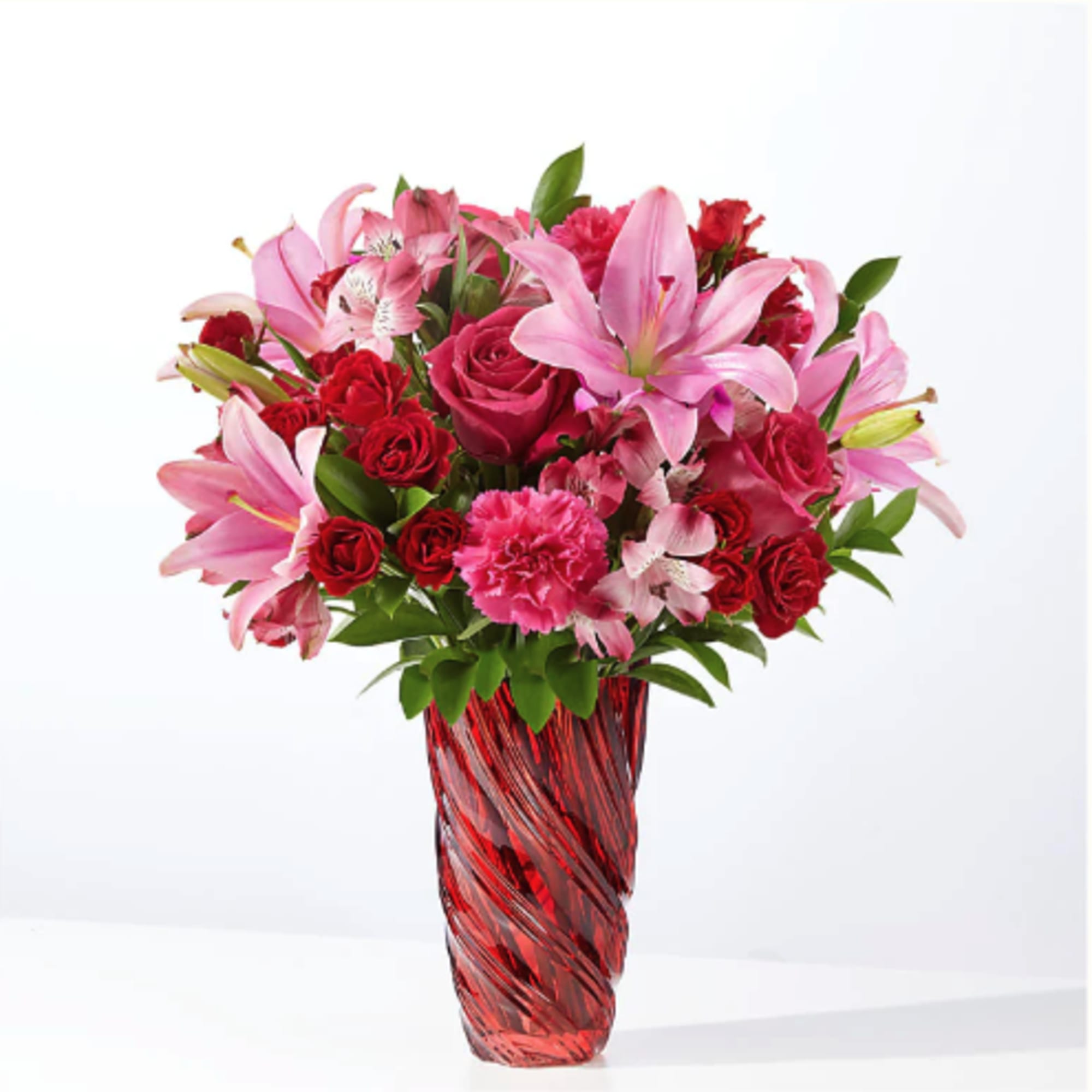 Pink lilies and red roses arranged in a red glass vase