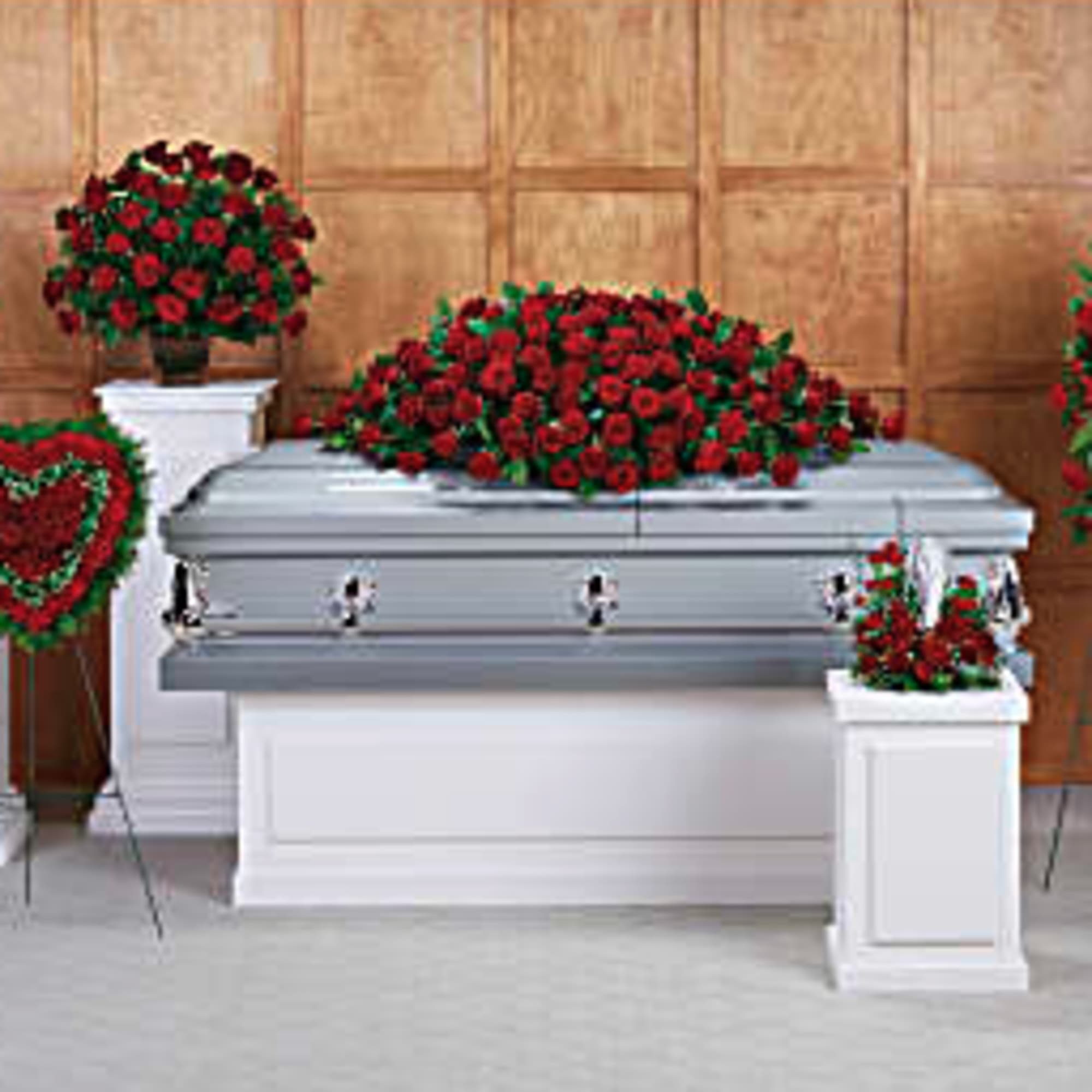 Casket surrounded by red rose funeral sprays and a heart wreath