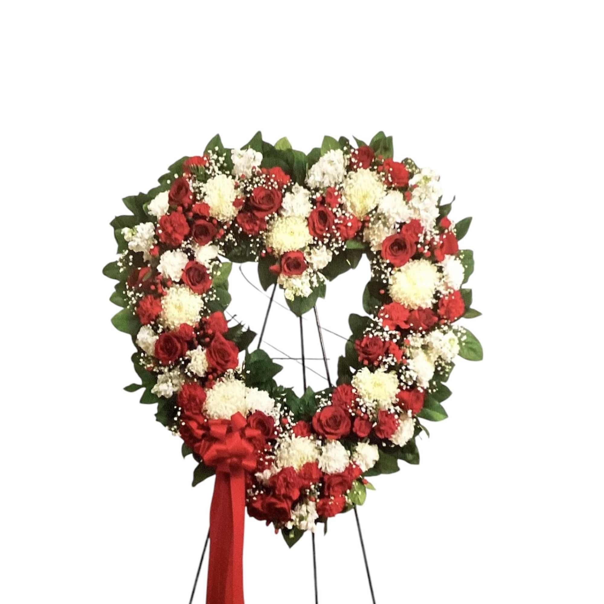 Heart-shaped floral wreath of red and white flowers on a stand with a red ribbon