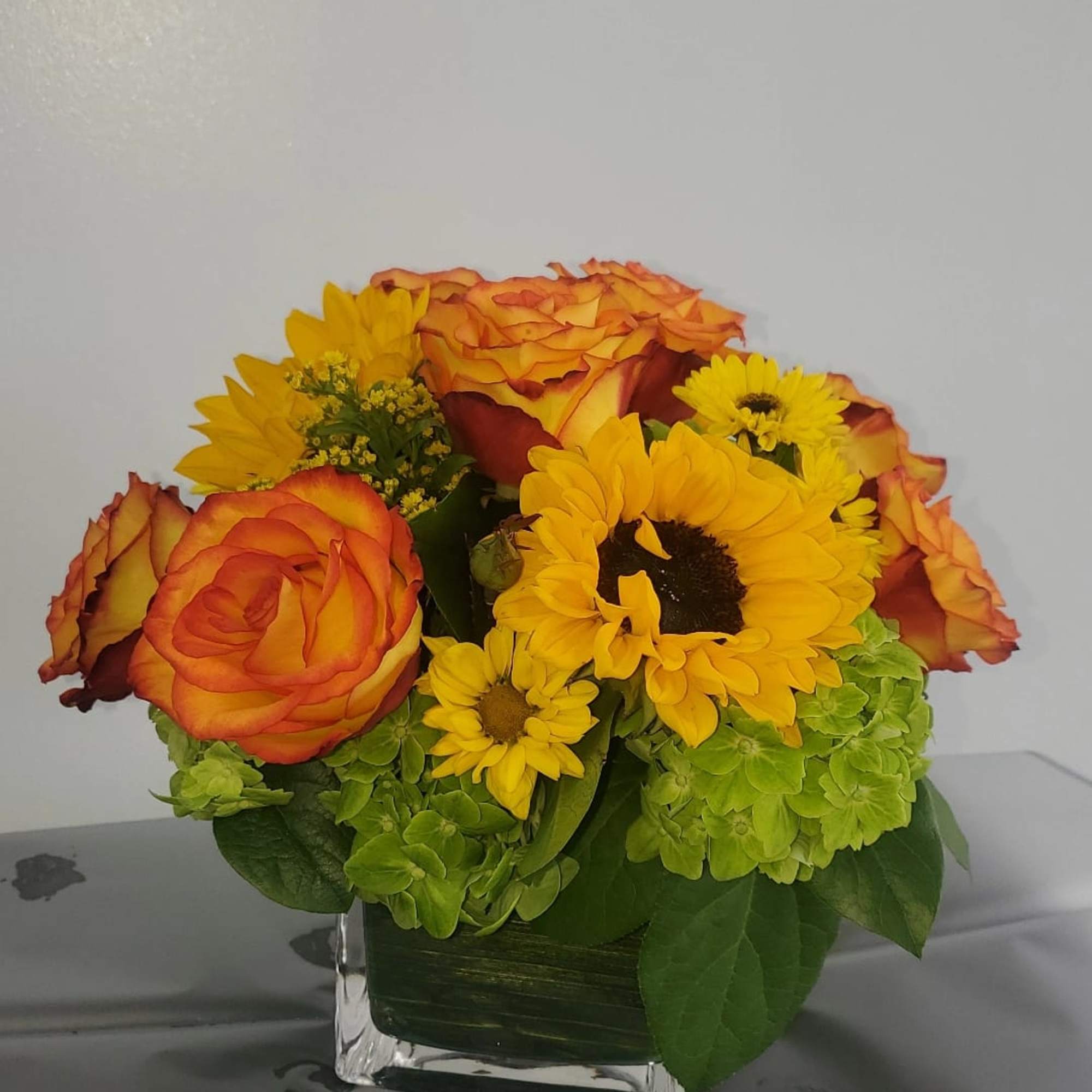 Orange roses and yellow sunflowers arranged in a square glass vase