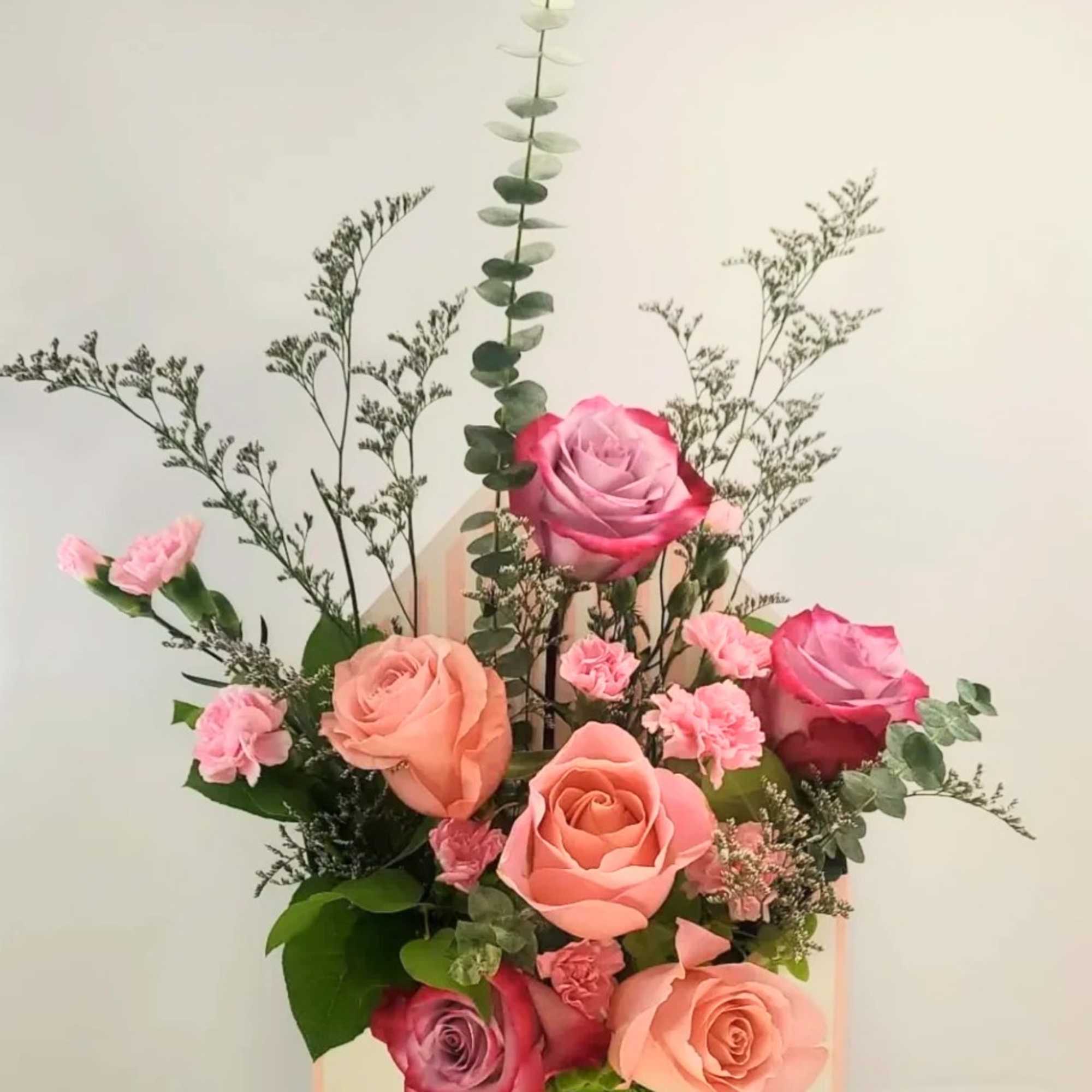 Pink and peach roses arranged in a pastel gift box with greenery