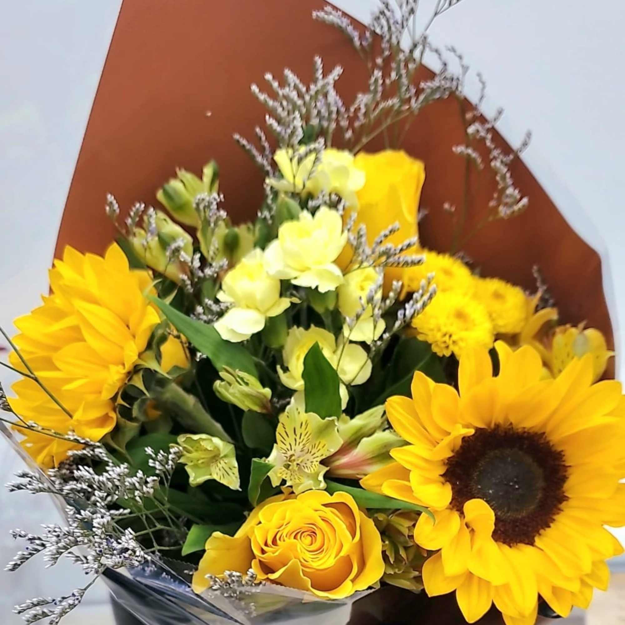 Bouquet of sunflowers, yellow roses, and pale yellow flowers in brown wrap