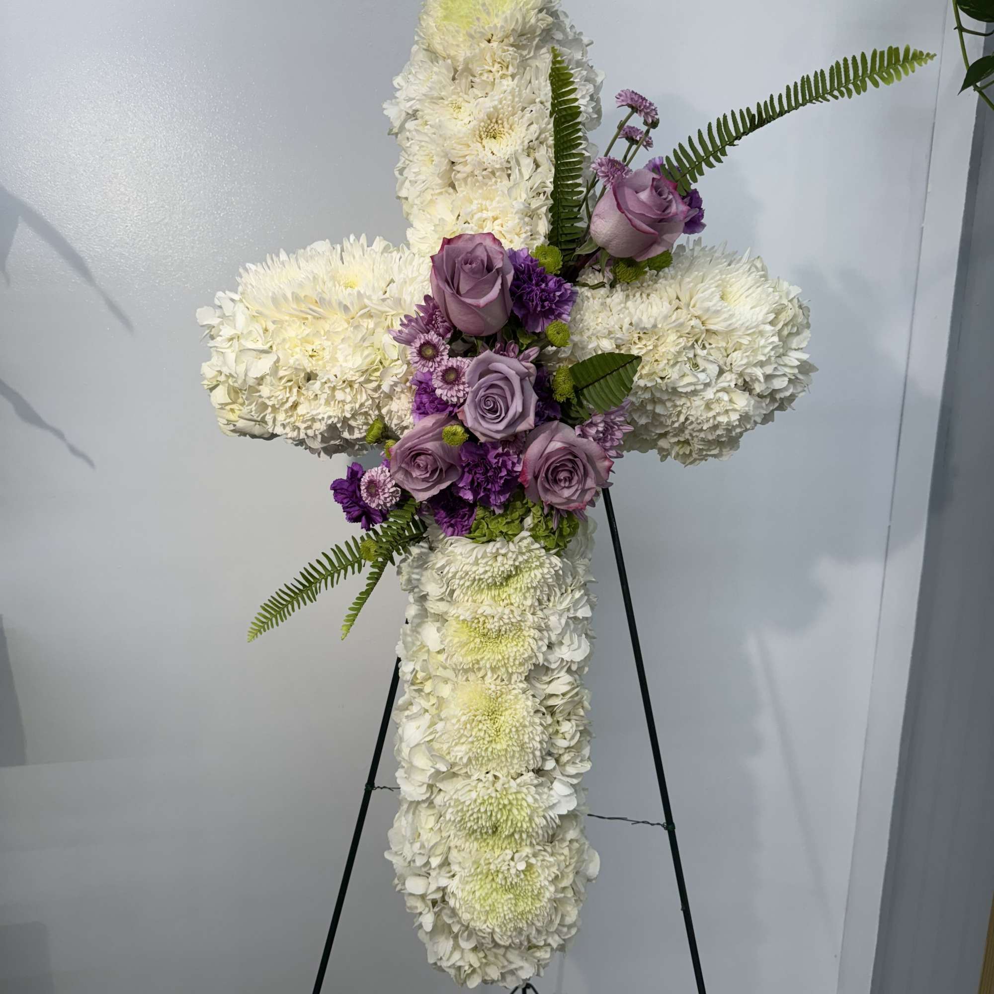 Cross-shaped floral tribute with white blooms and lavender roses on an easel