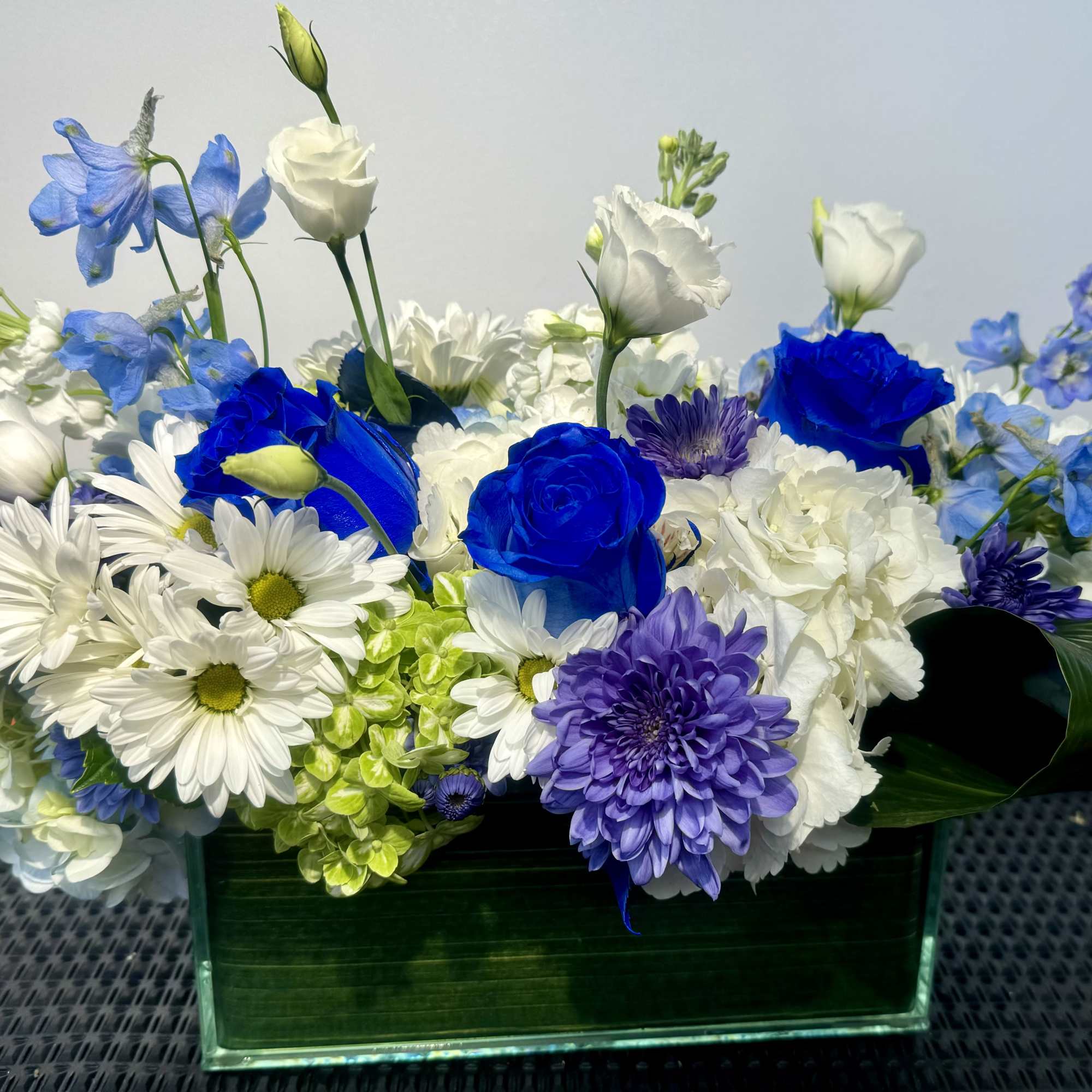 Blue, white, and purple flowers arranged in a rectangular glass vase