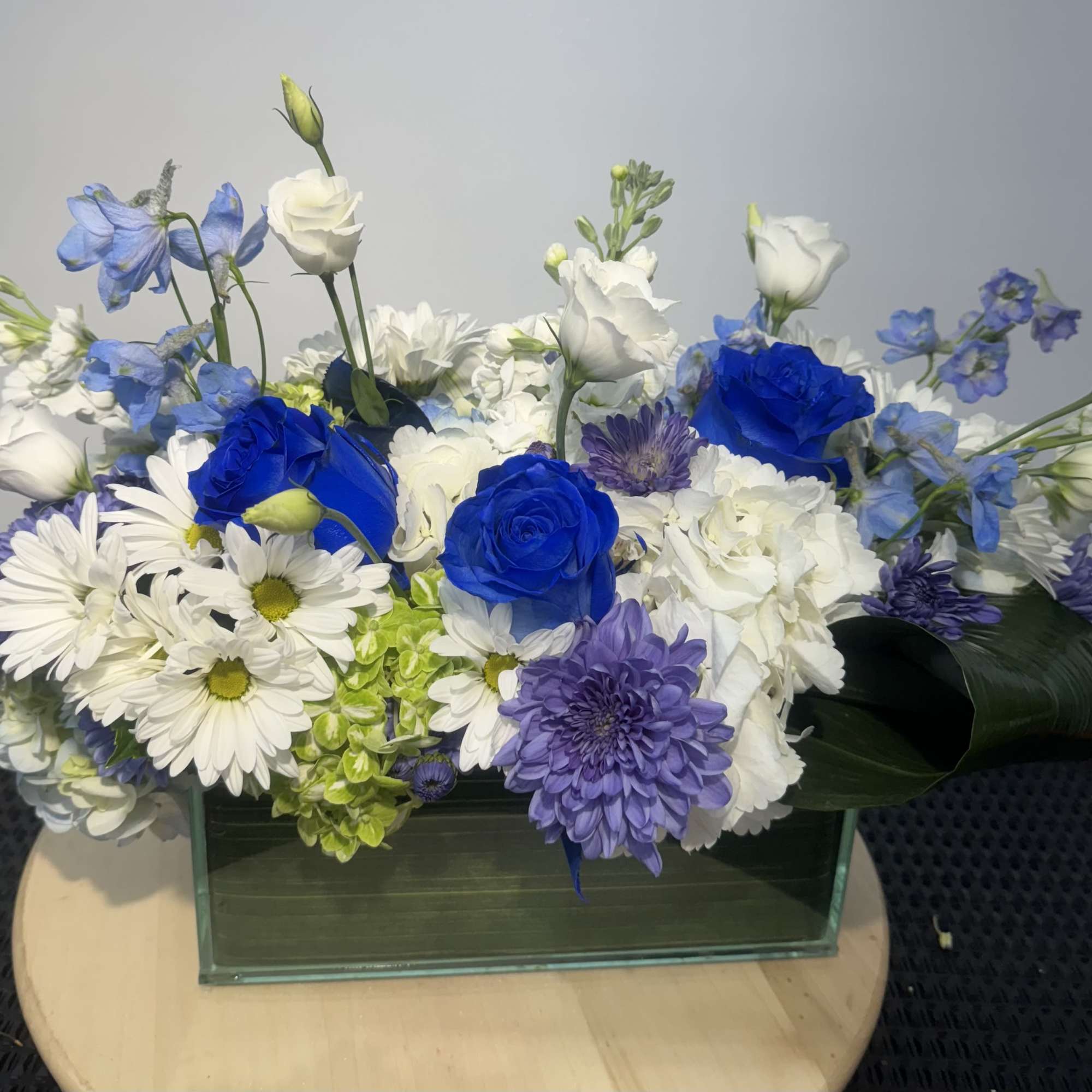 Blue, white, and purple floral arrangement in a rectangular glass vase