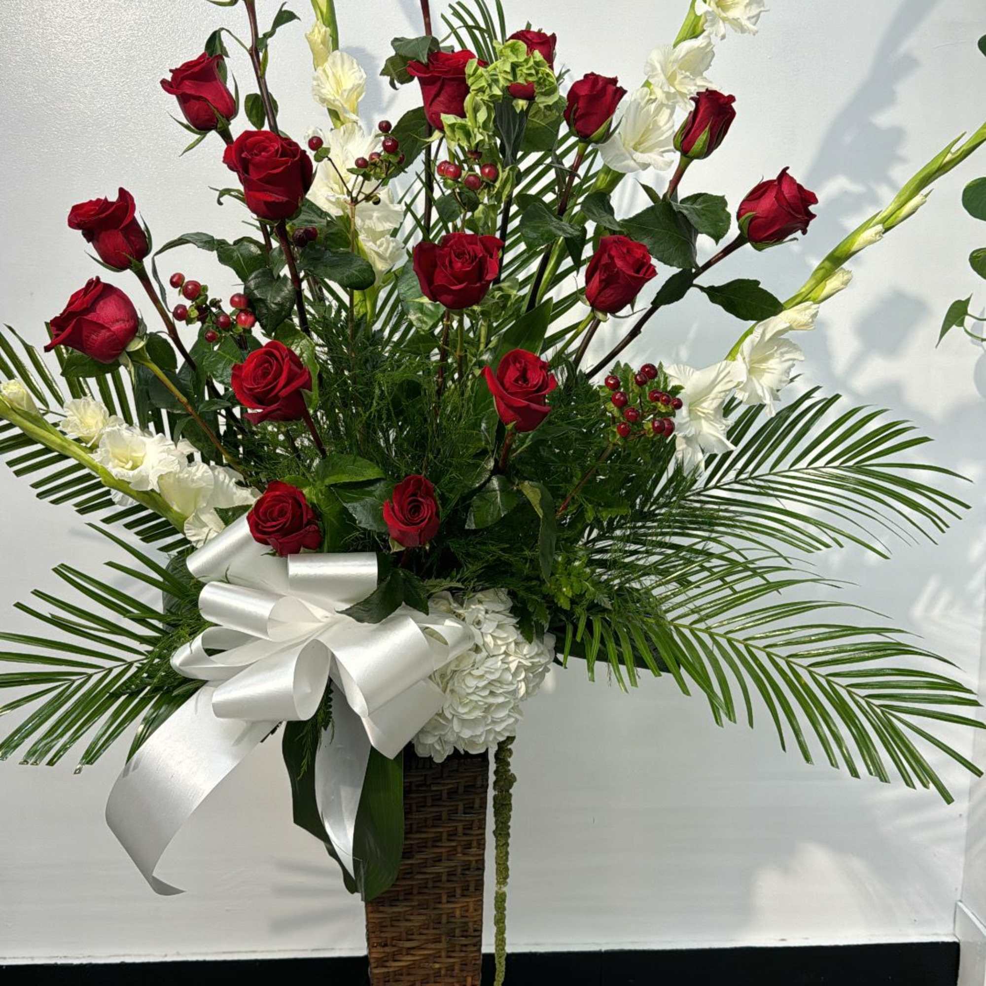 Tall floral arrangement with red roses and white flowers in a wicker pedestal vase