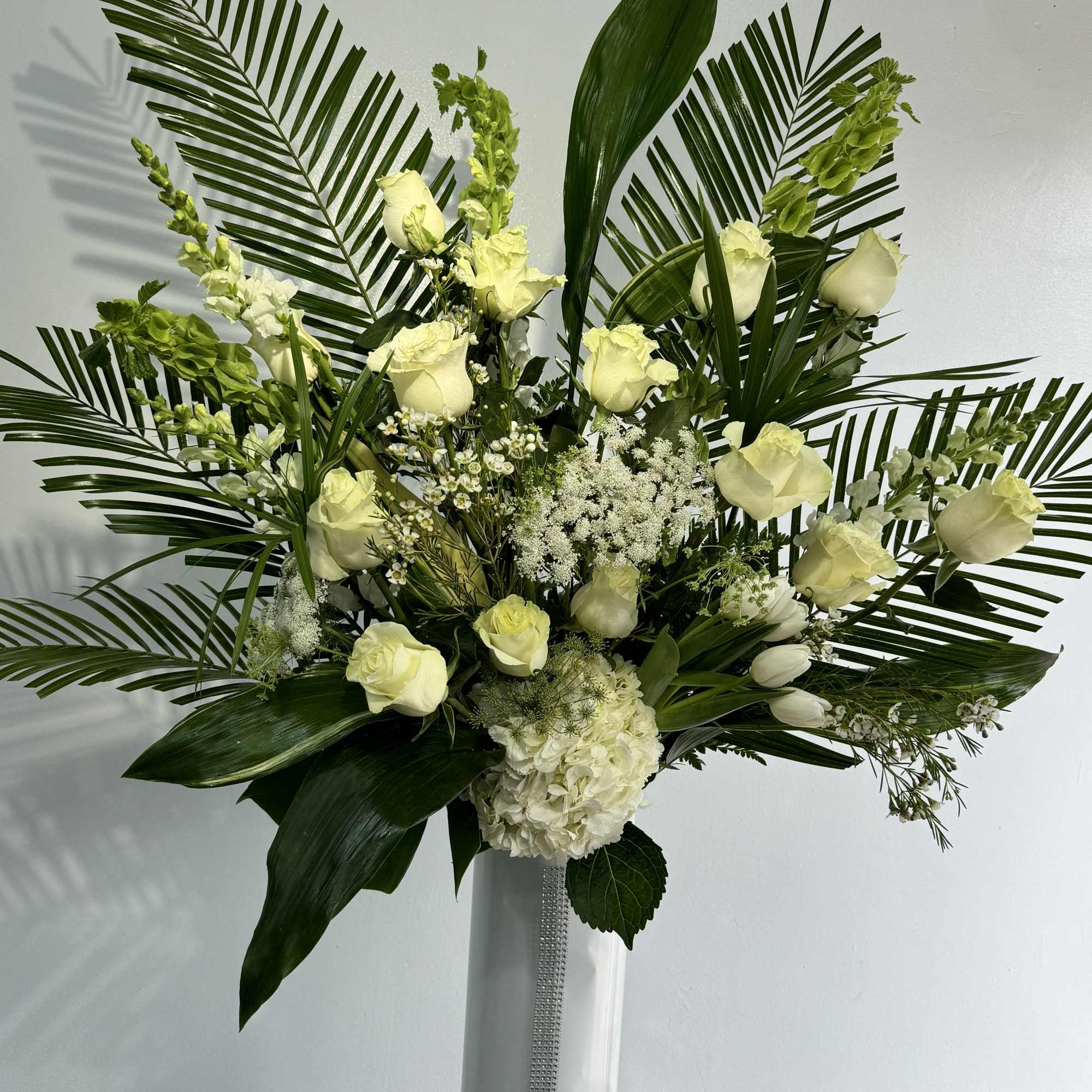 Tall white rose arrangement with palm fronds in a white vase